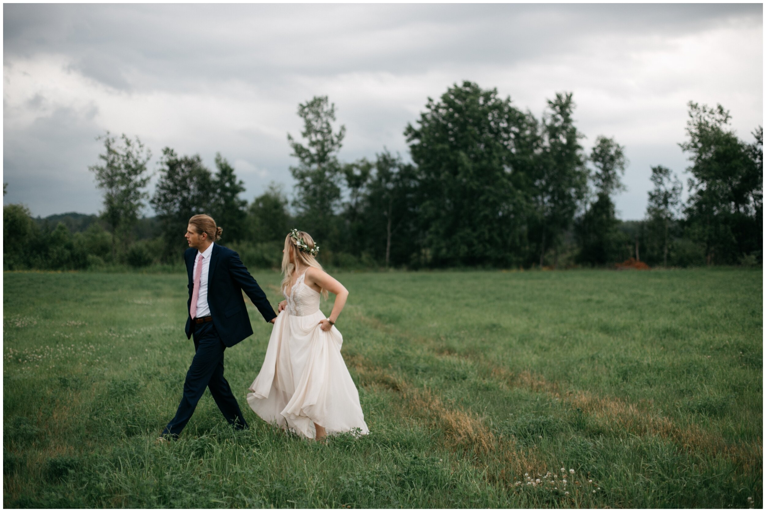 Bride and groom walking in field with stormy sky in background during Northern Pacific Center wedding