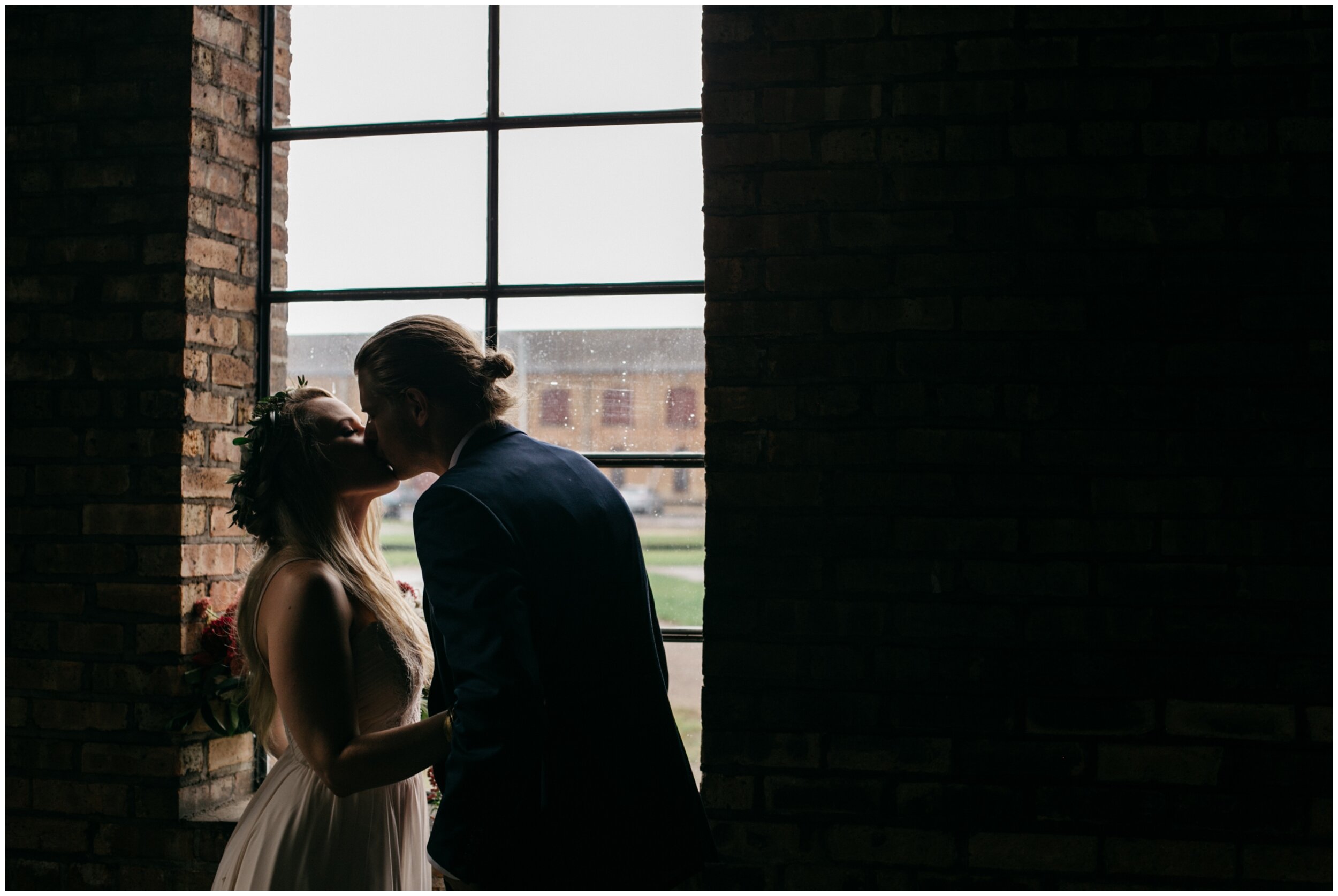 Bride and groom kissing in front of window in industrial warehouse wedding at the Northern Pacific Center