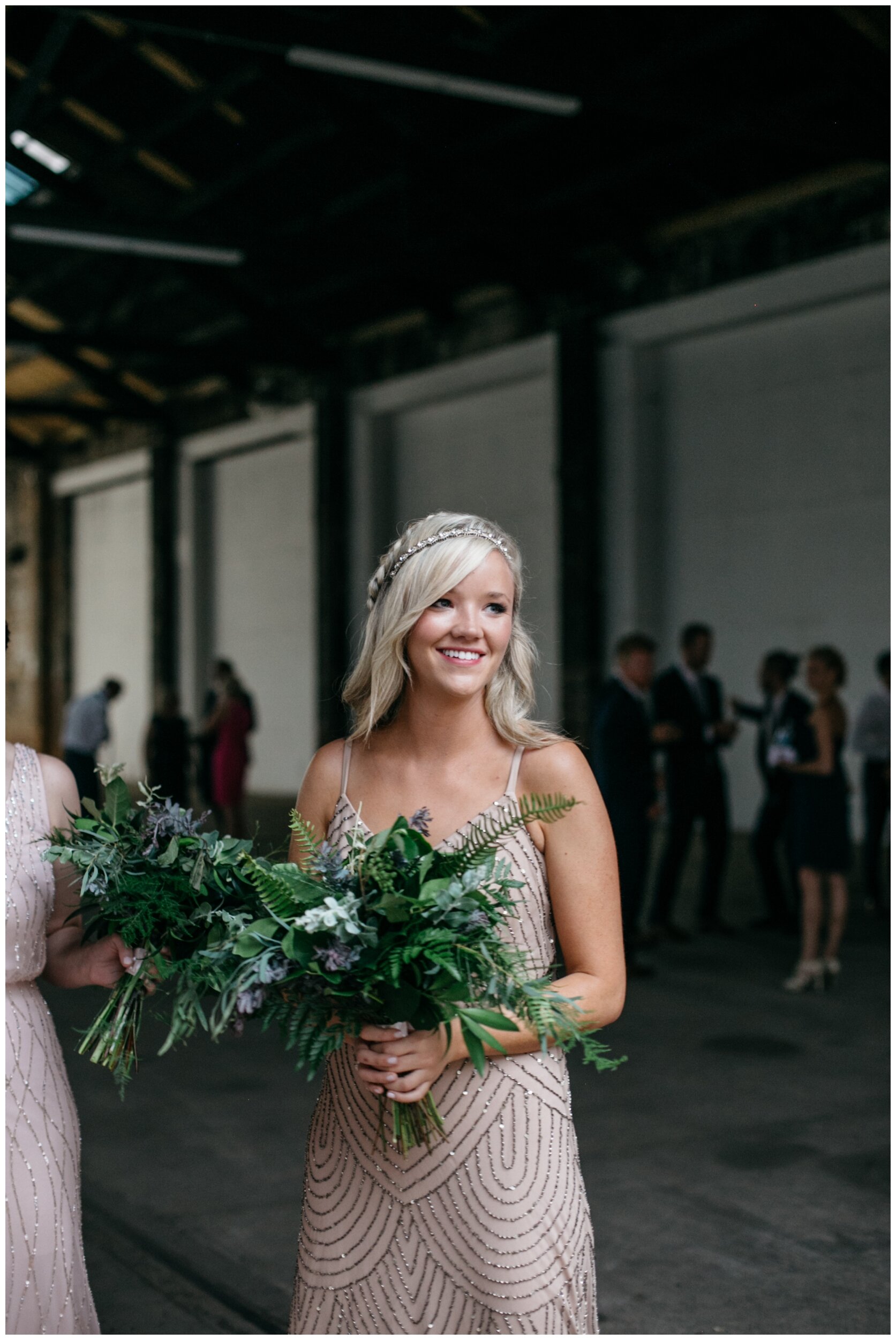 Bridesmaid wearing blush dress with gold sequins holding fern bouquet