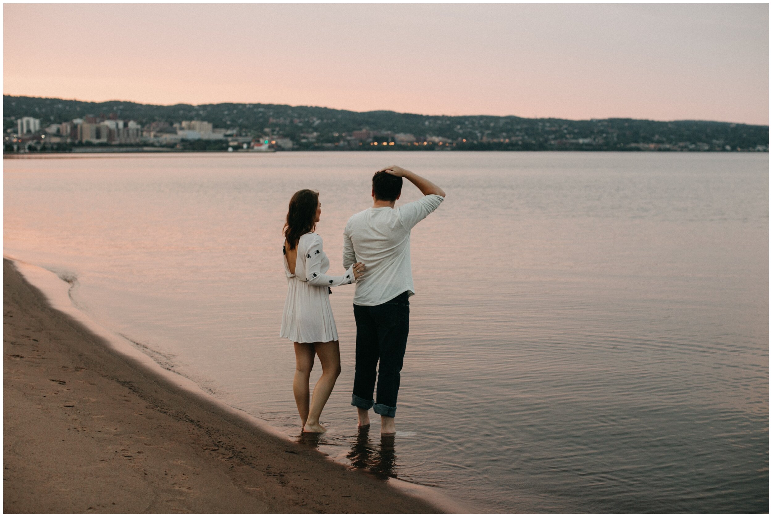 Couple standing along shore of Lake Superior during sunset engagement session in Duluth, Minnesota