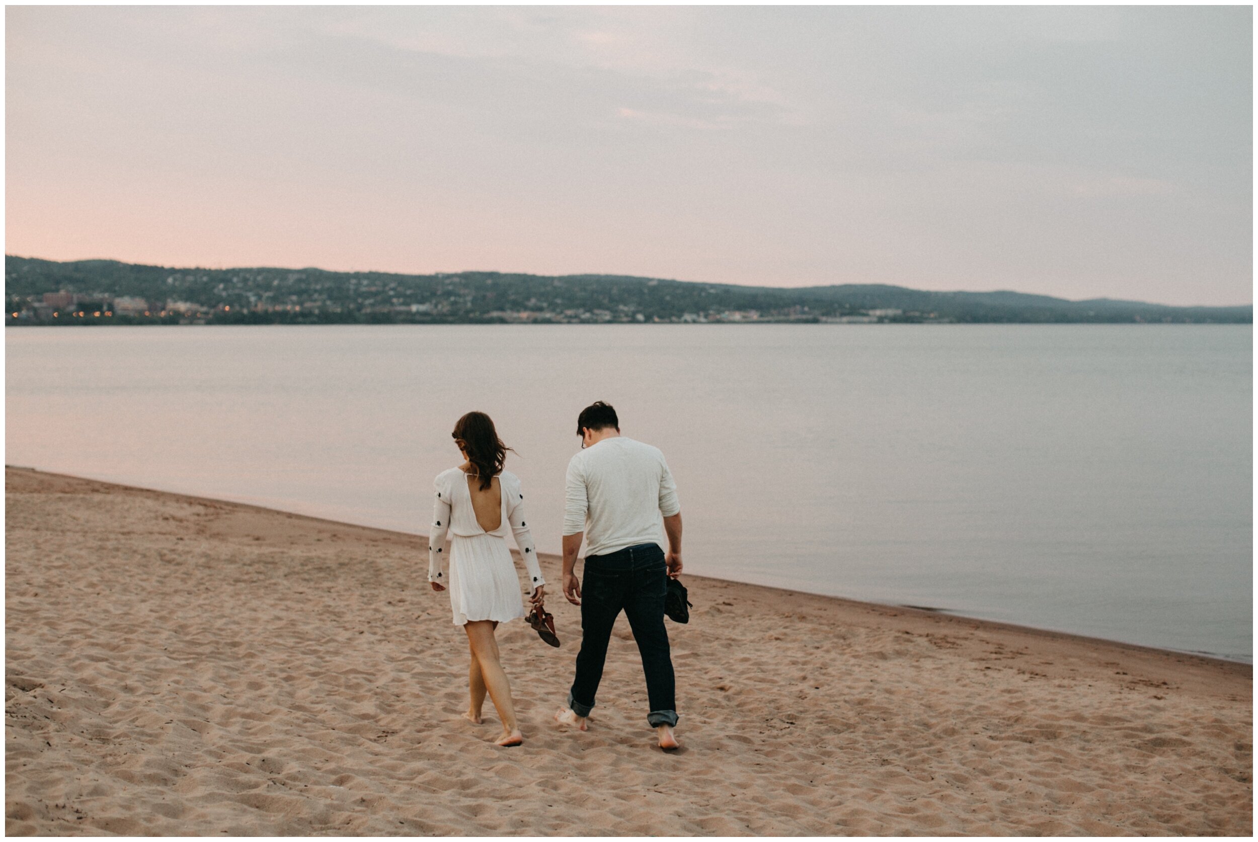 Couple walking along Park Point beach during sunset engagement session in Duluth, MN