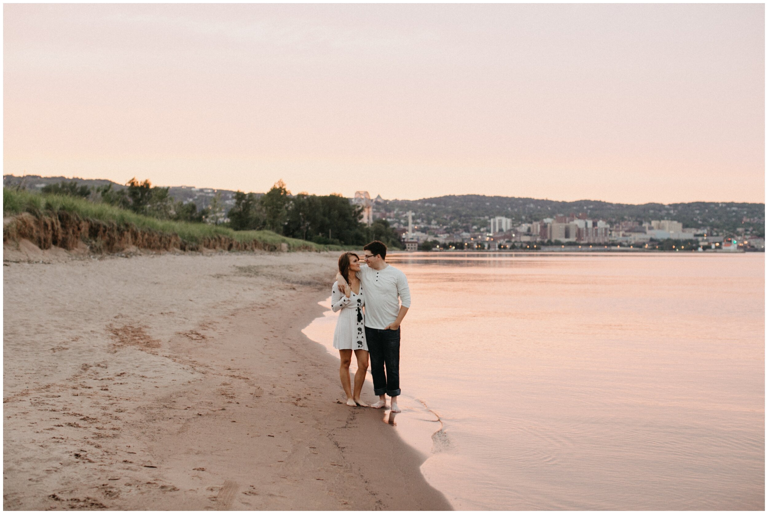 Couple walking on sandy beach during sunset engagement session in Duluth, Minnesota