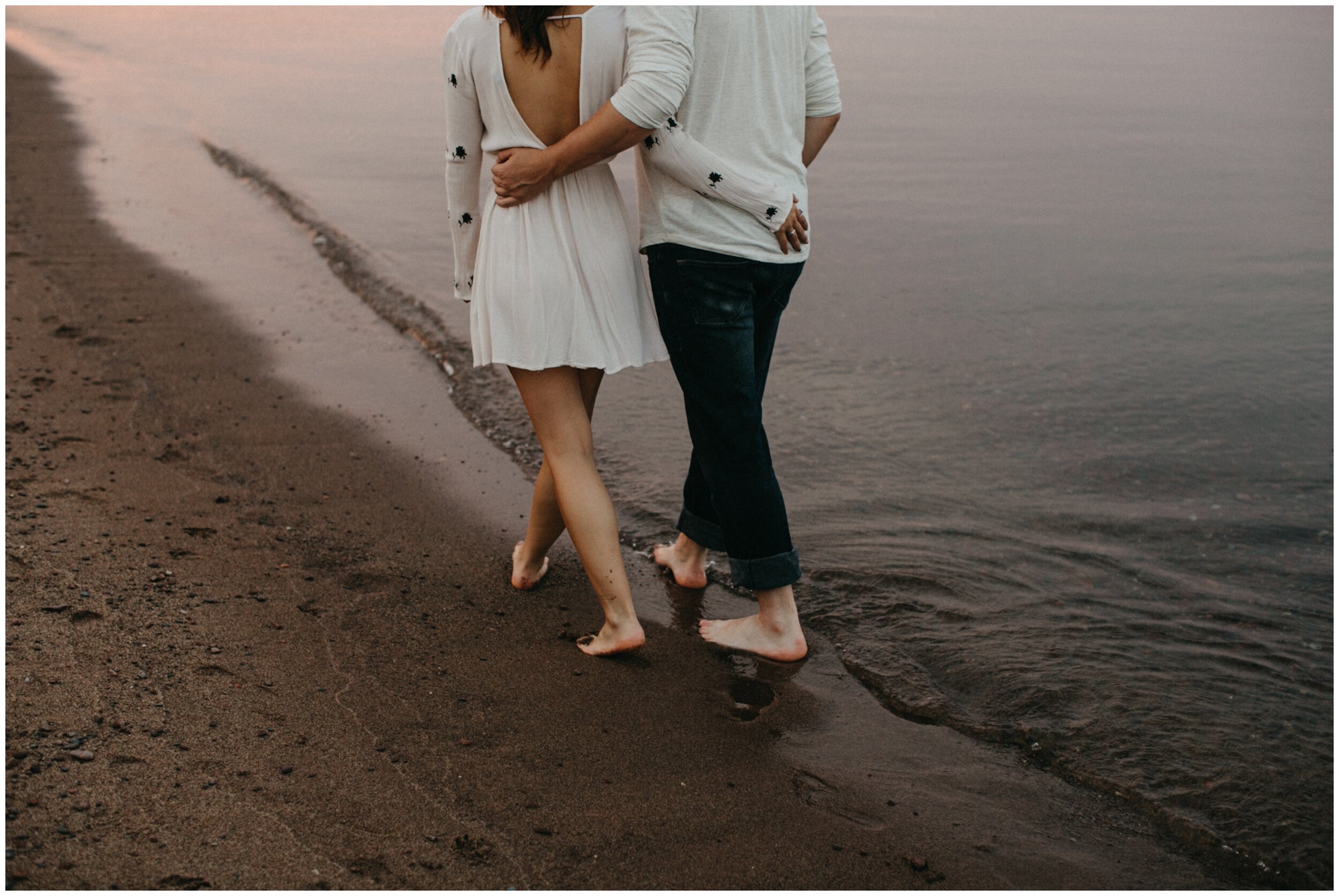 Couple walking along lake superior north shore beach during sunset engagement session in Duluth, Minnesota