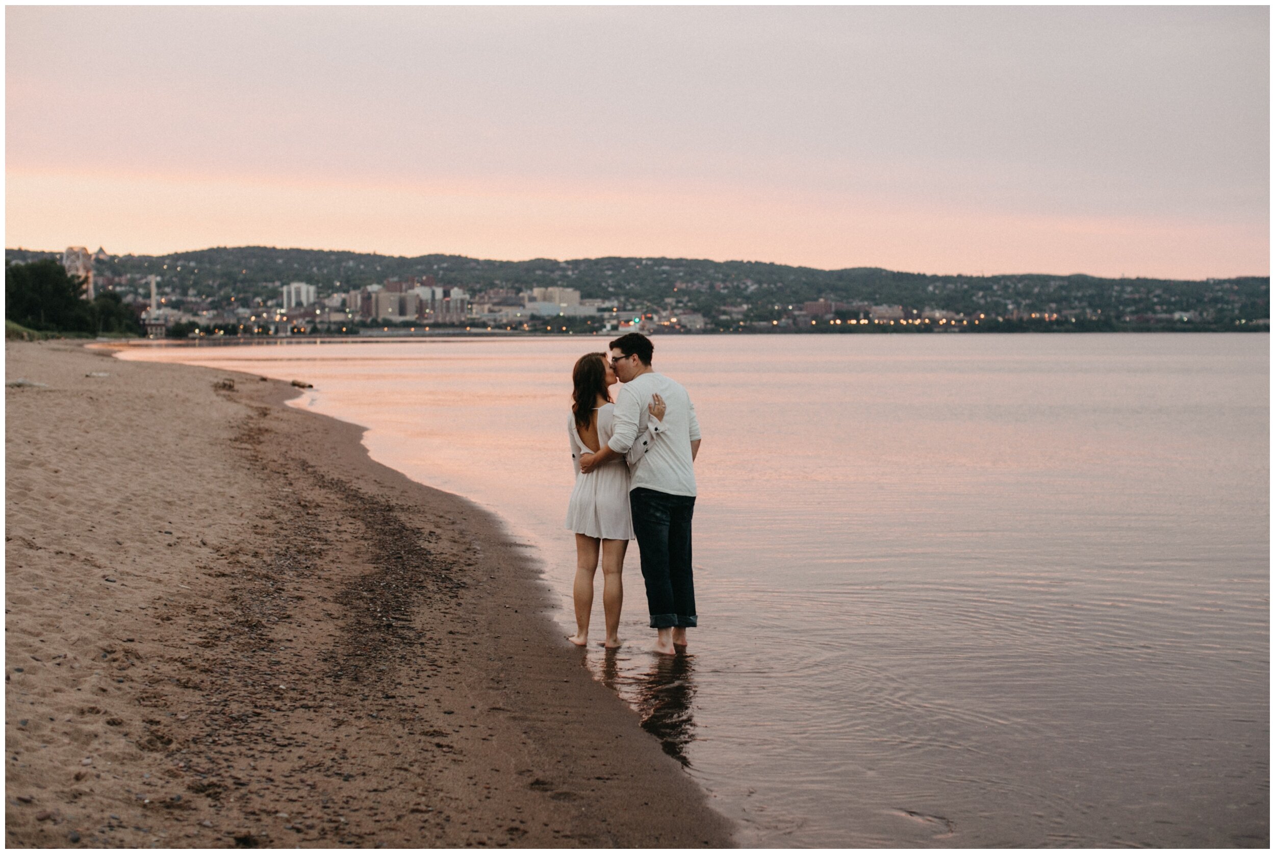 Couple kissing on beach during sunset engagement session at Park Point Beach in Duluth, MN
