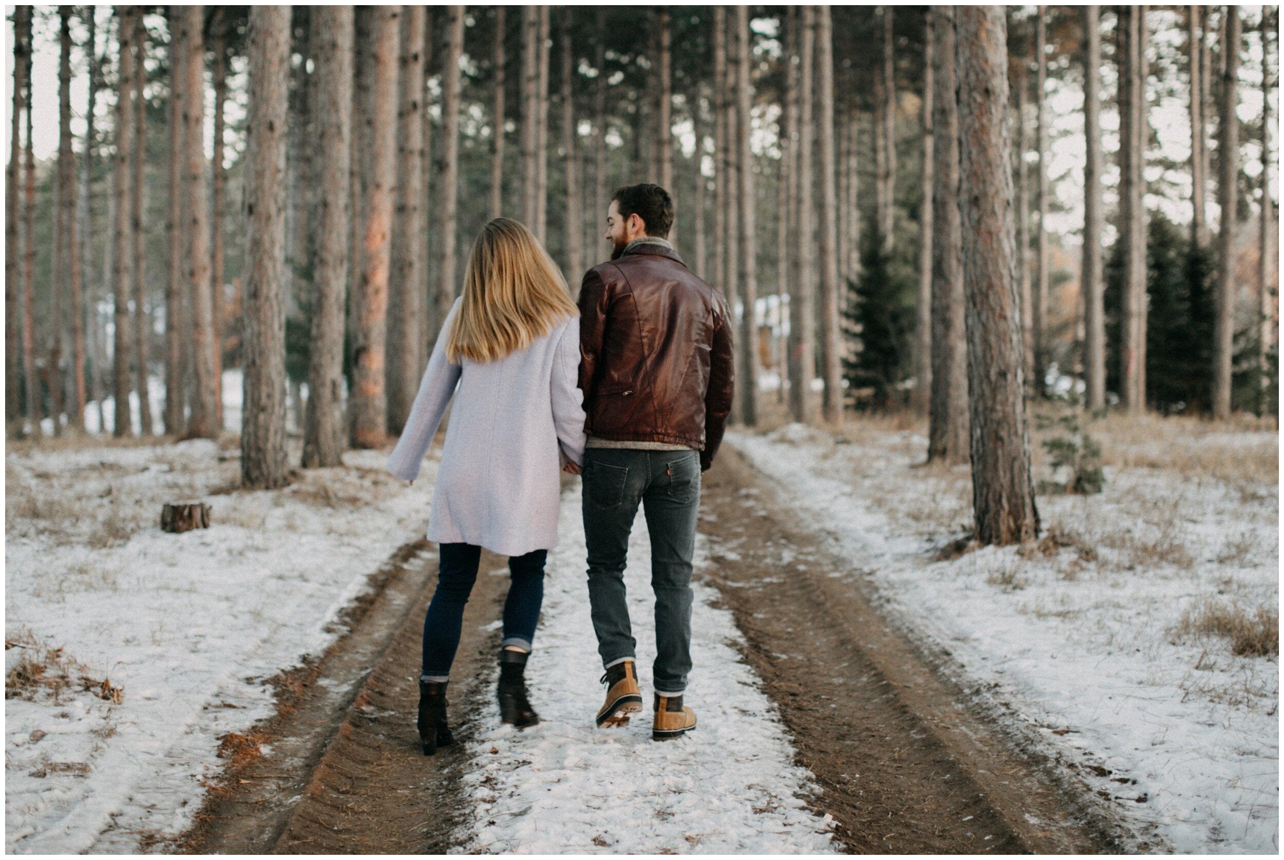 Couple walking through pine tree forest during engagement session at Minnesota Christmas tree farm