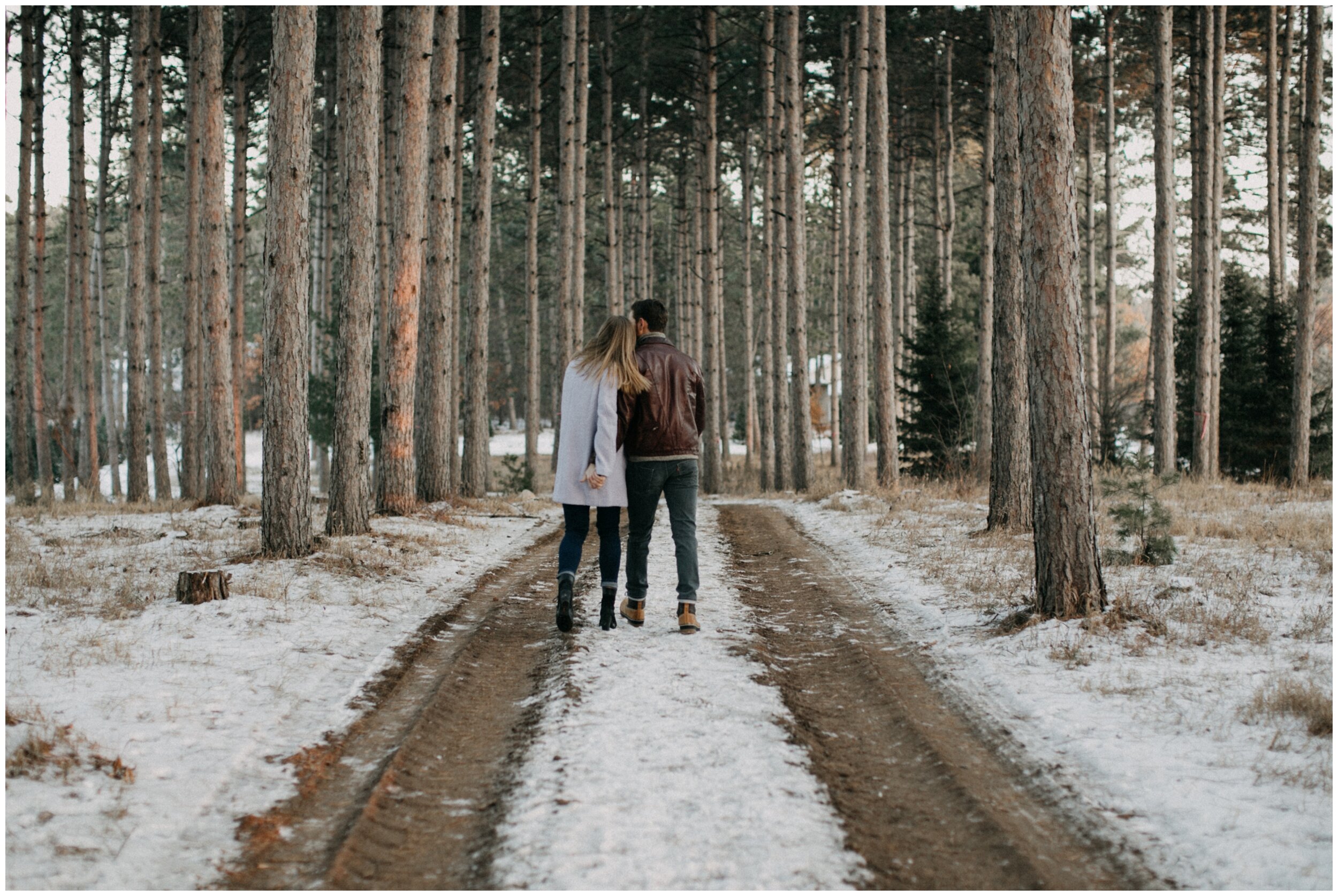 Couple walking through pine tree forest in the snow during winter at Minnesota Christmas tree farm