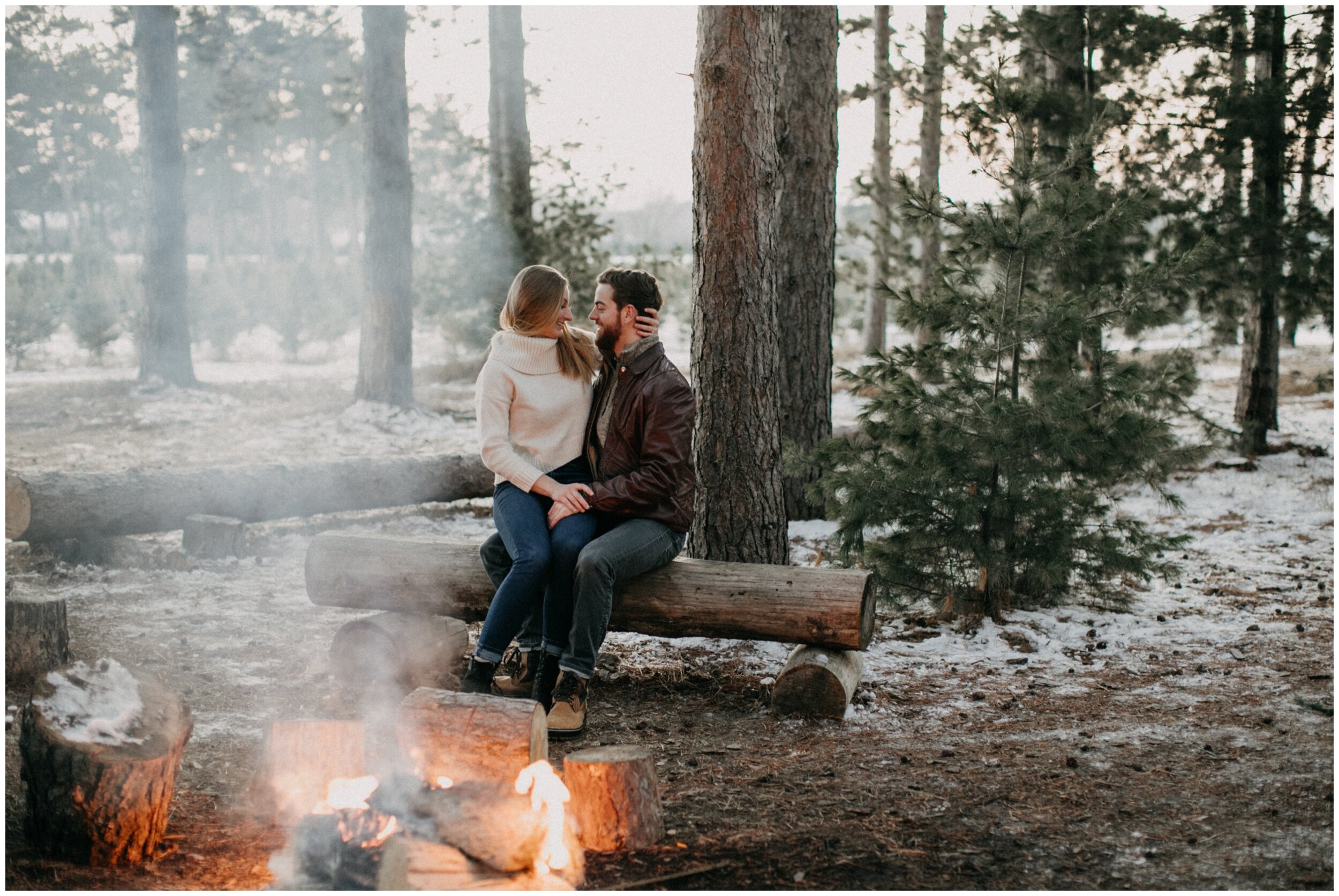 Couple sitting at winter bonfire during engagement session at Minnesota Christmas tree farm
