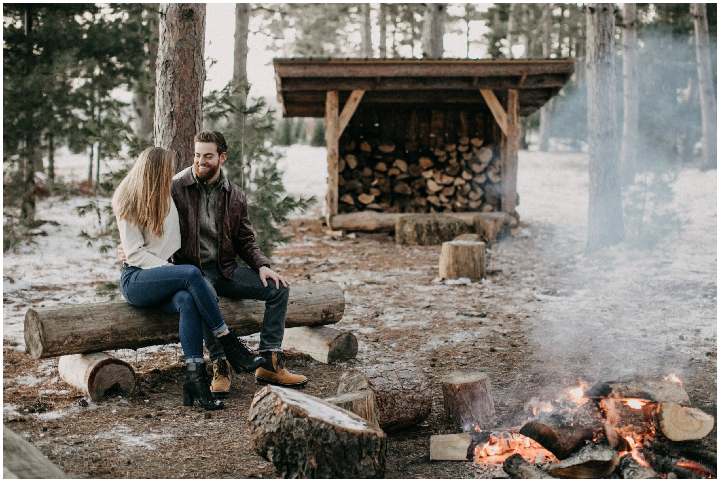 Couple sitting by fire at Minnesota Christmas tree farm during engagement session