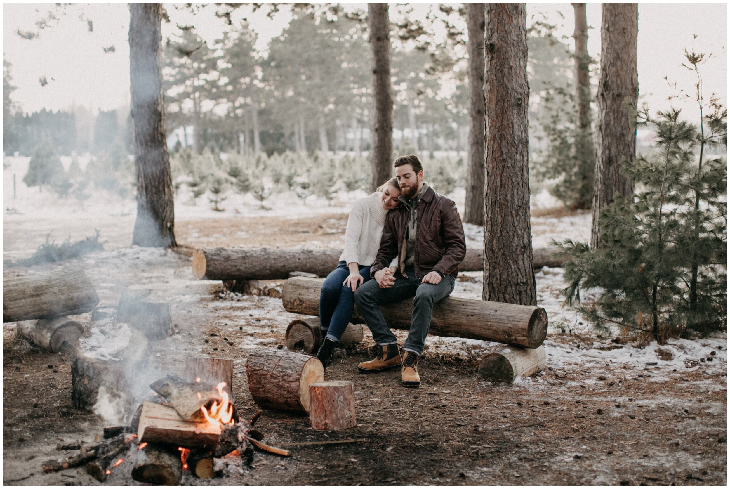 Couple having a winter bonfire during engagement session at Hansen Christmas Tree farm in Minnesota