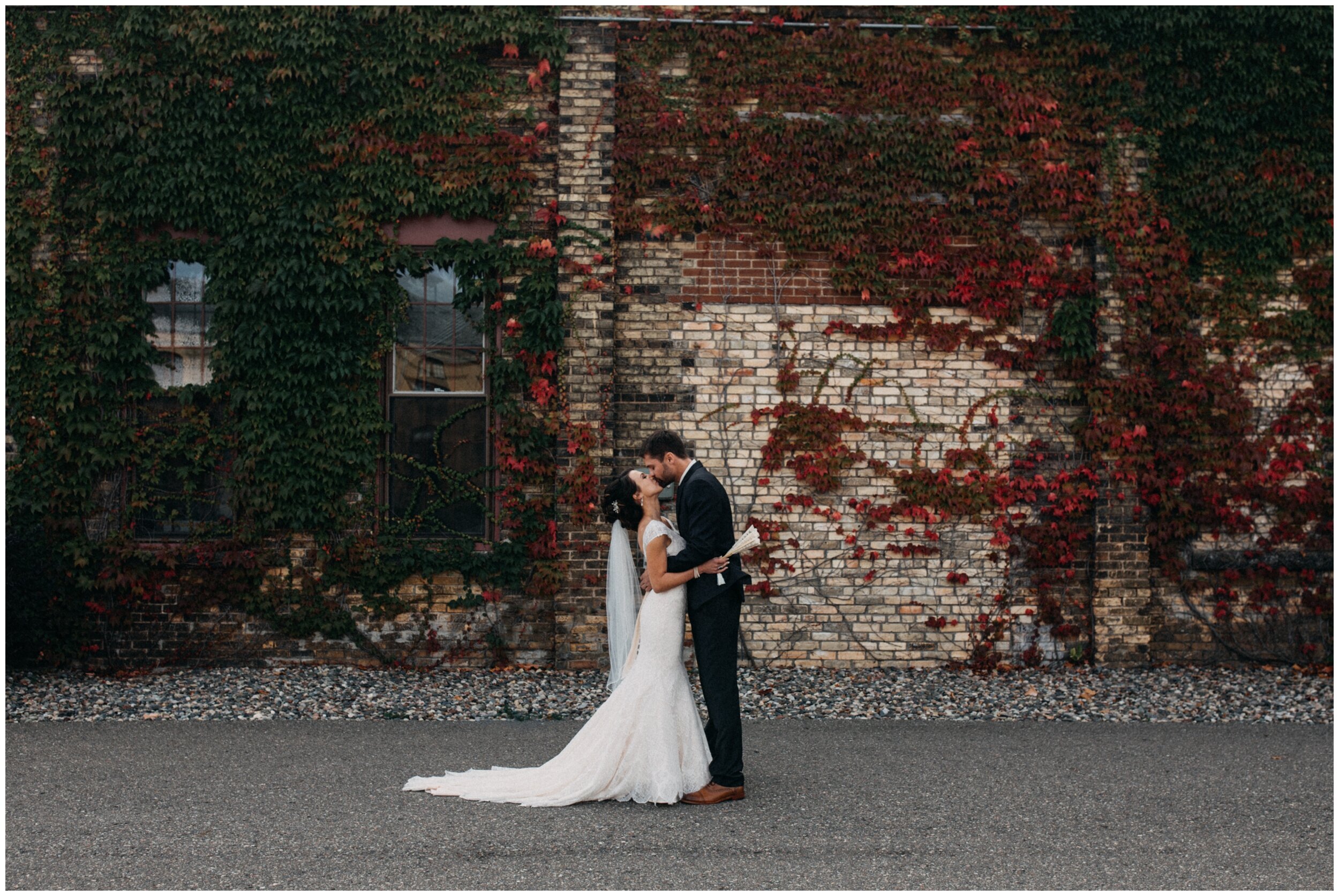 Bride and groom kissing in front of industrial ivy, brick wall during fall wedding at the Northern Pacific Center in Brainerd, Minnesota