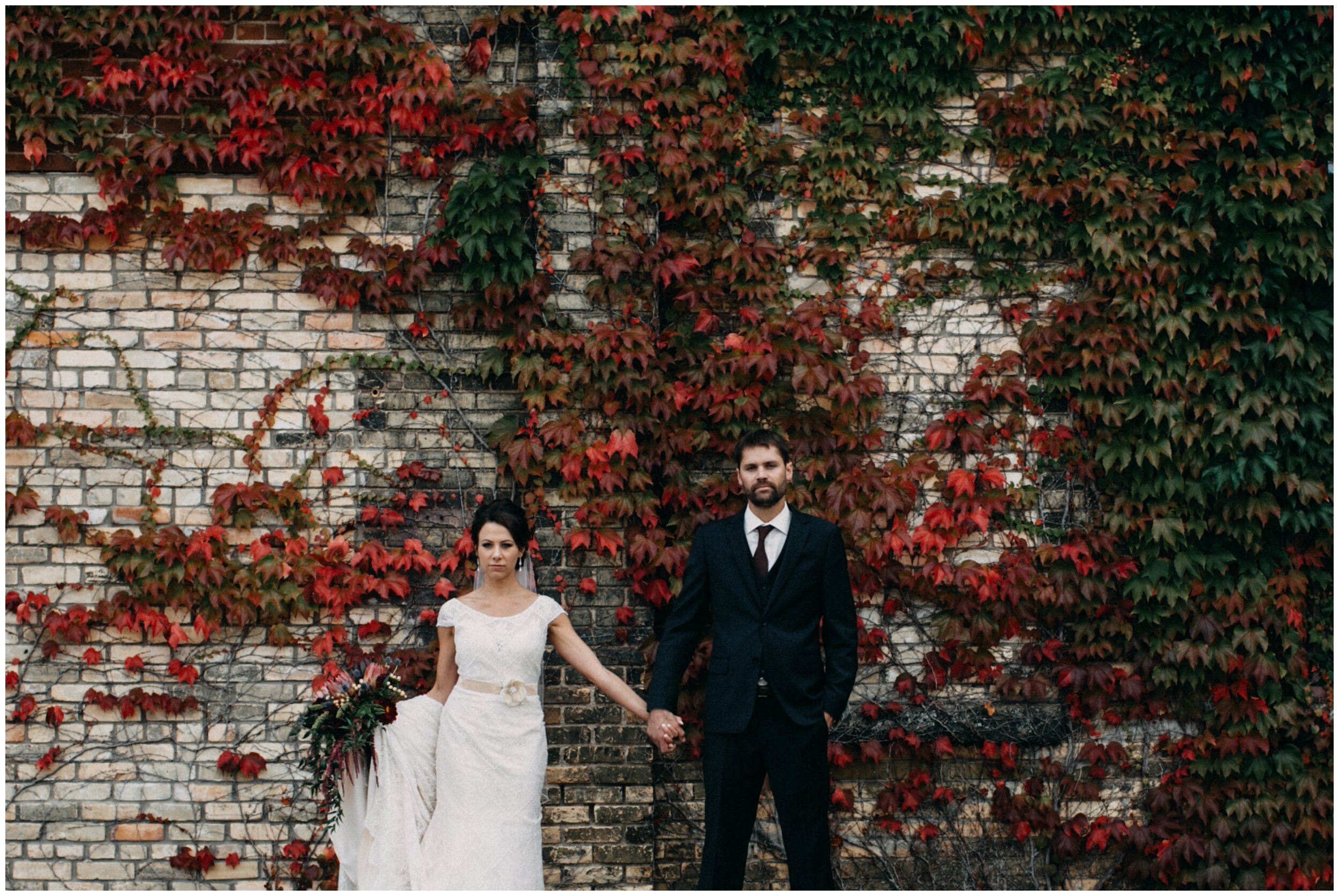 Bride and groom holding hands, standing in front of warehouse wall covered in ivy during fall wedding at the Northern Pacific Center in Brainerd, Minnesota