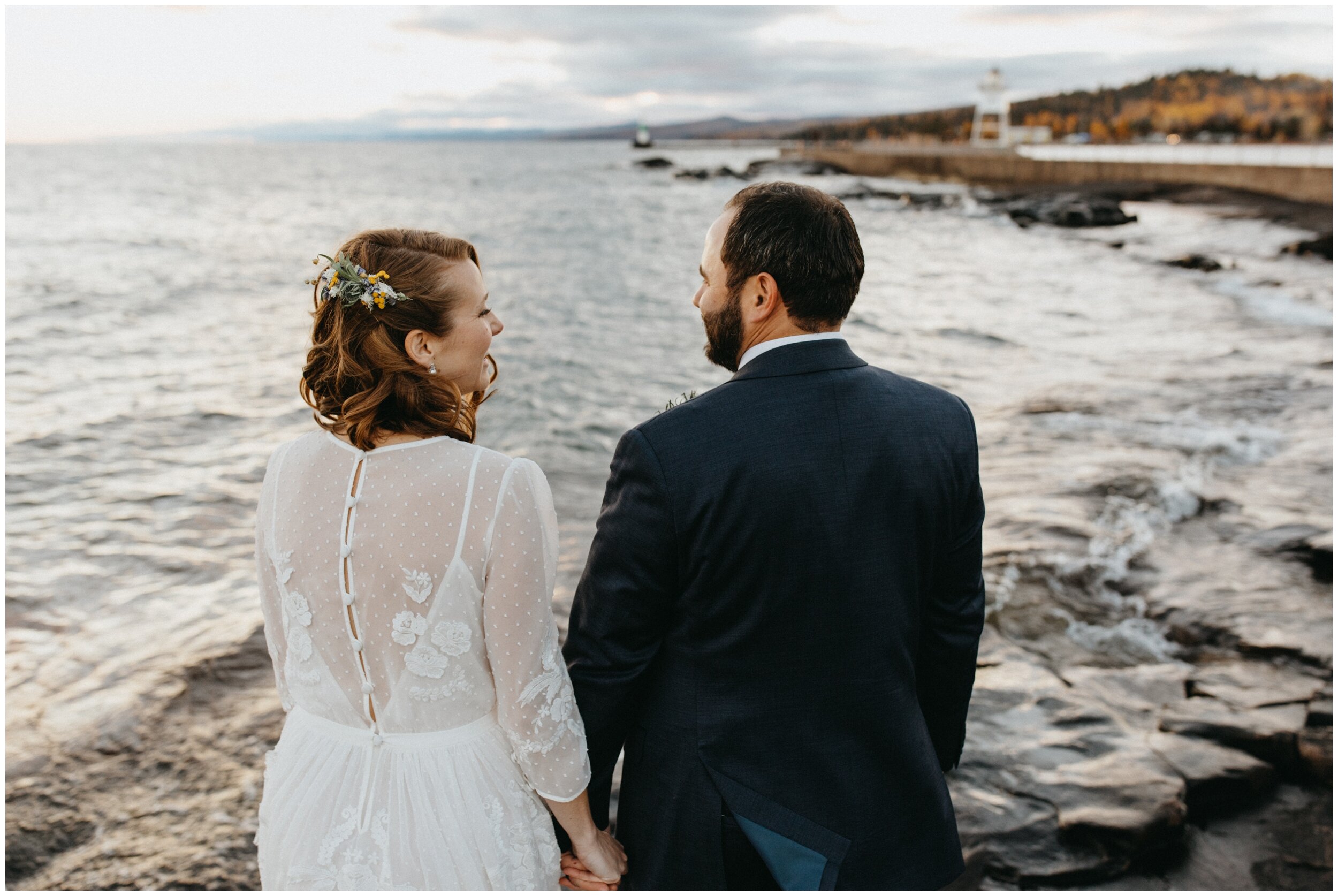 Bride and groom holding hands looking out at the sunset on Lake Superior in Grand Marias, Minnesota