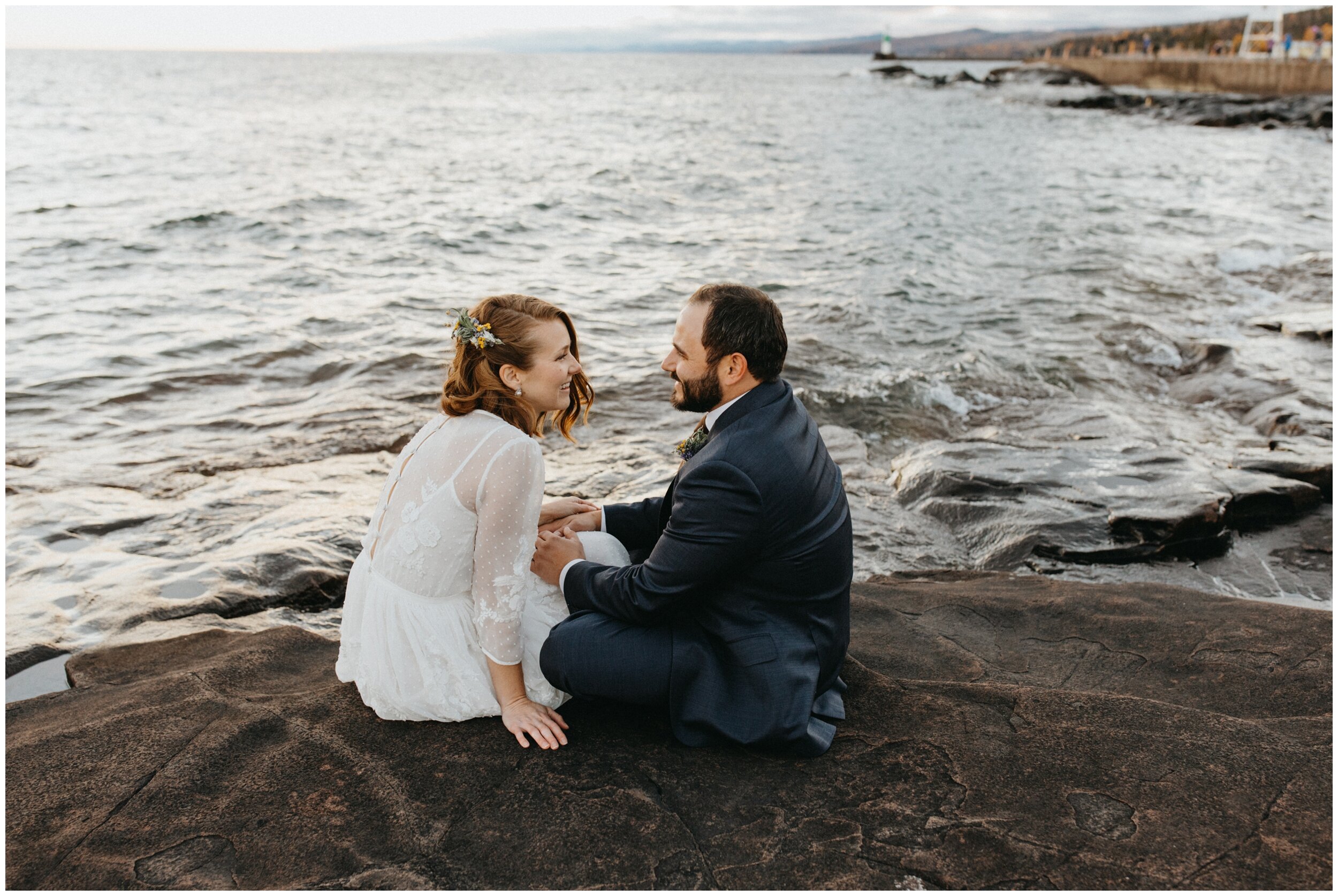 Bride and groom sitting on the north shore, during sunset during Artists' Point wedding in Grand Marais, Minnesota