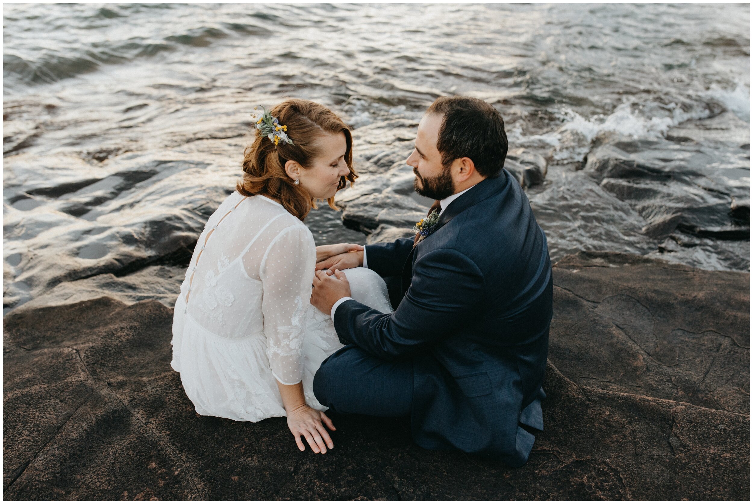 Bride and groom sitting on rocky Artists' Point after Grand Marais, Minnesota wedding