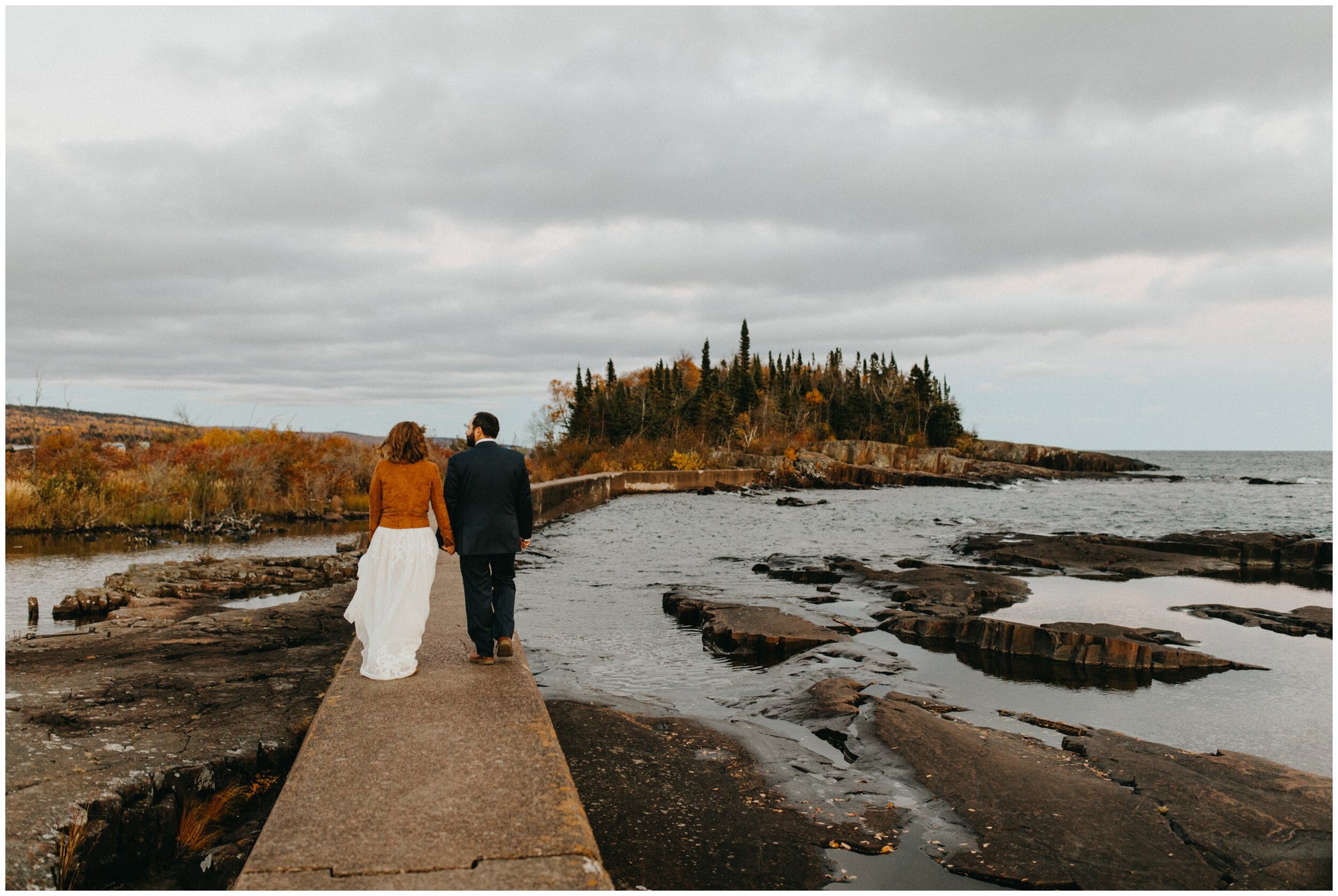Bride and groom walking on Artists' Point boardwalk after fall wedding in Grand Marais, MN