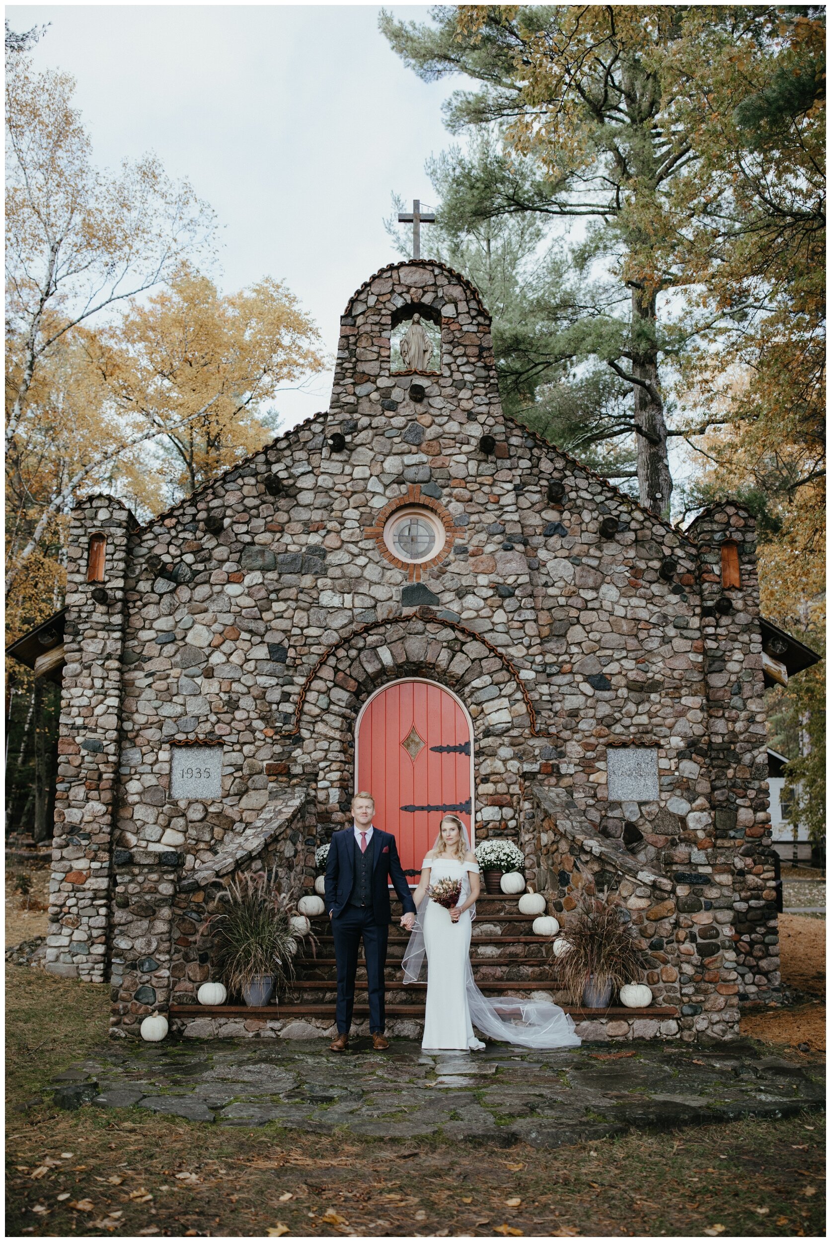 Bride and groom standing in front of chapel in the woods at fall wedding on Crosslake, Minnesota
