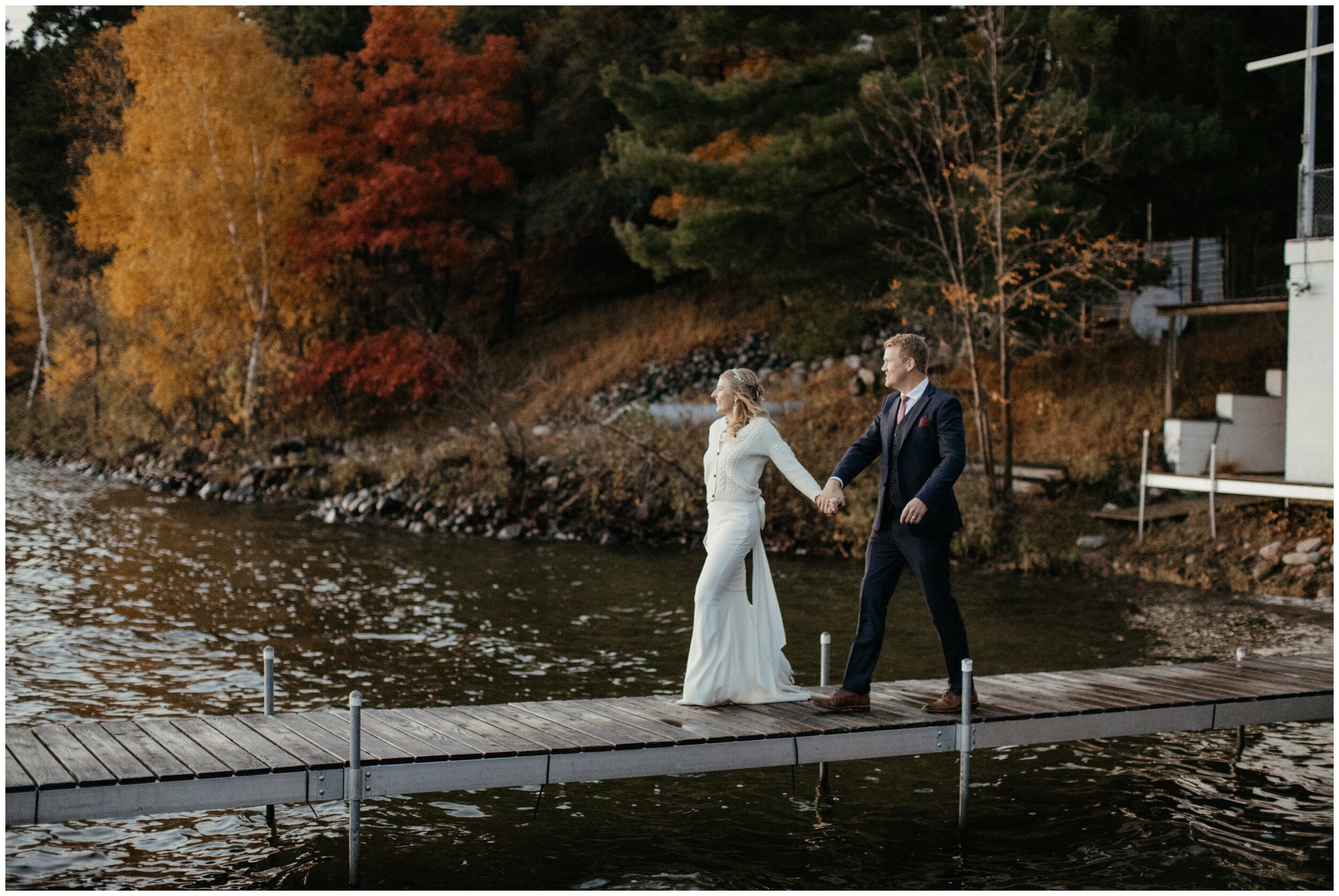 Bride and groom walking on dock on Crosslake during fall wedding at Camp Foley