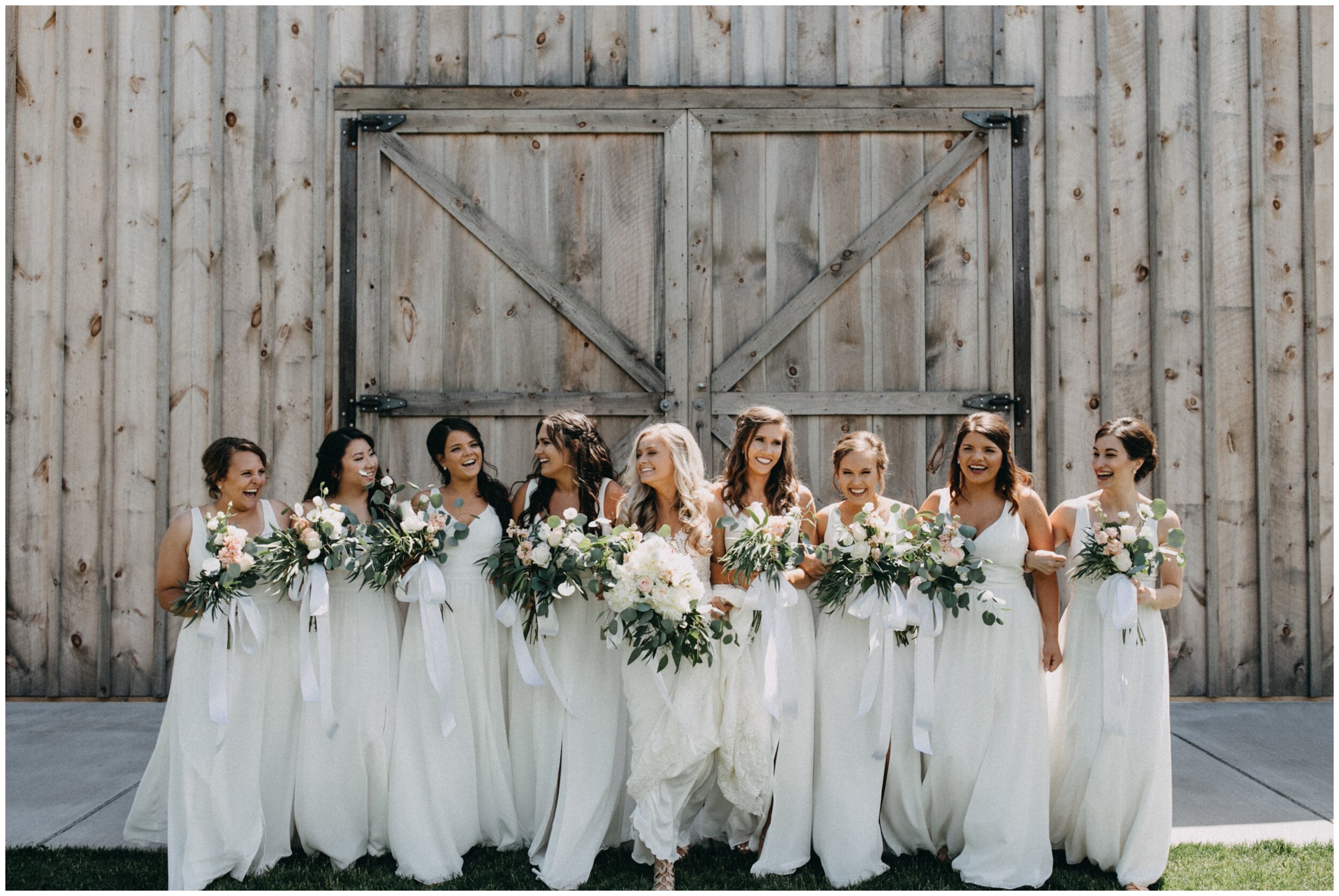 Bridesmaids wearing white dresses walking with bride outside barn at Creekside Farm in Rush City, Minnesota