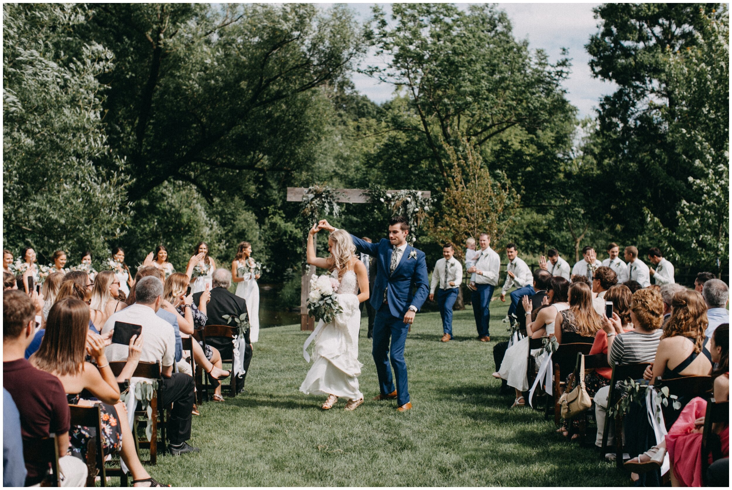 Groom spinning bride as they dance down aisle after outdoor barn wedding ceremony in Minnesota