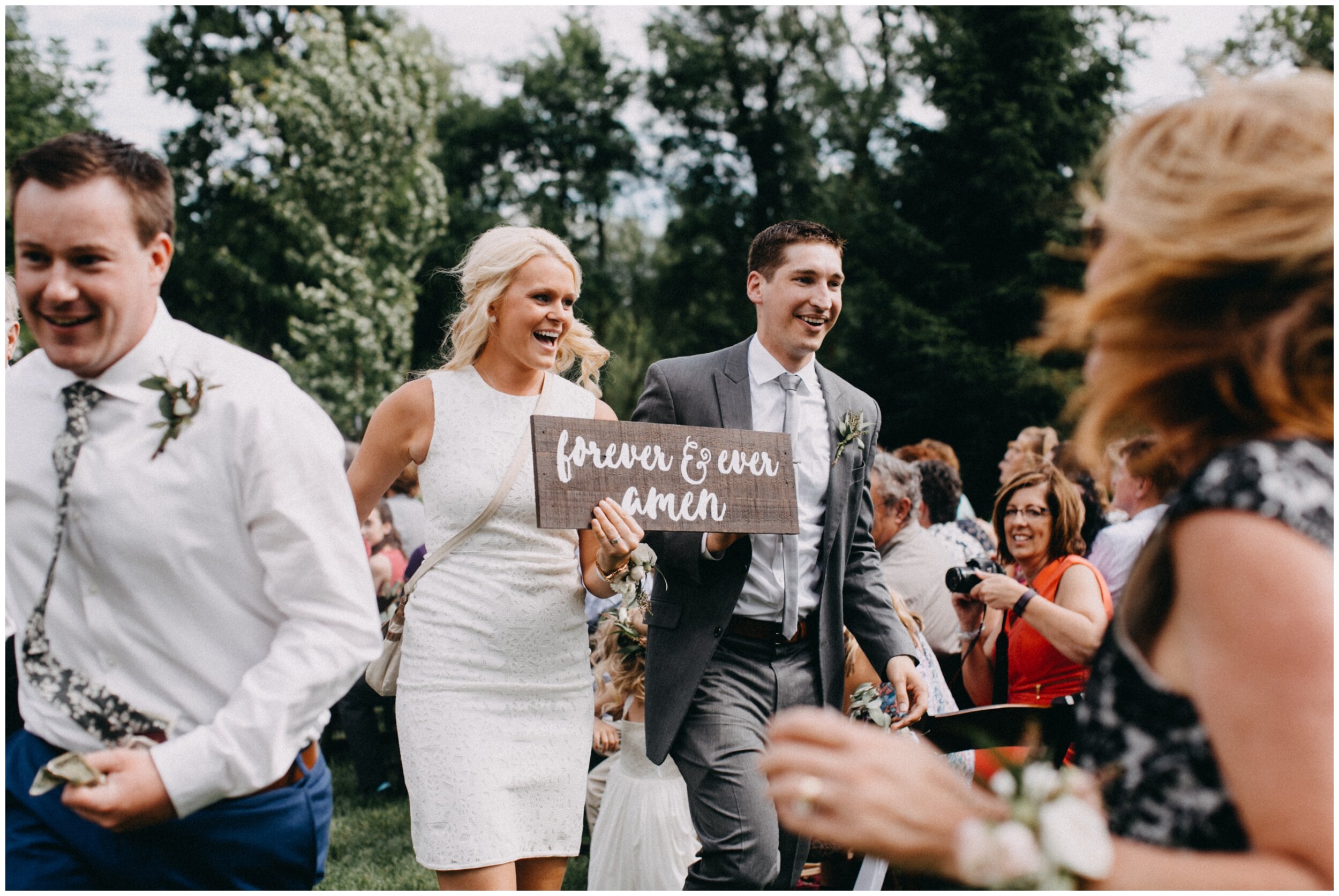 Bridesmaid and groomsman walking down aisle holding happily ever after sign