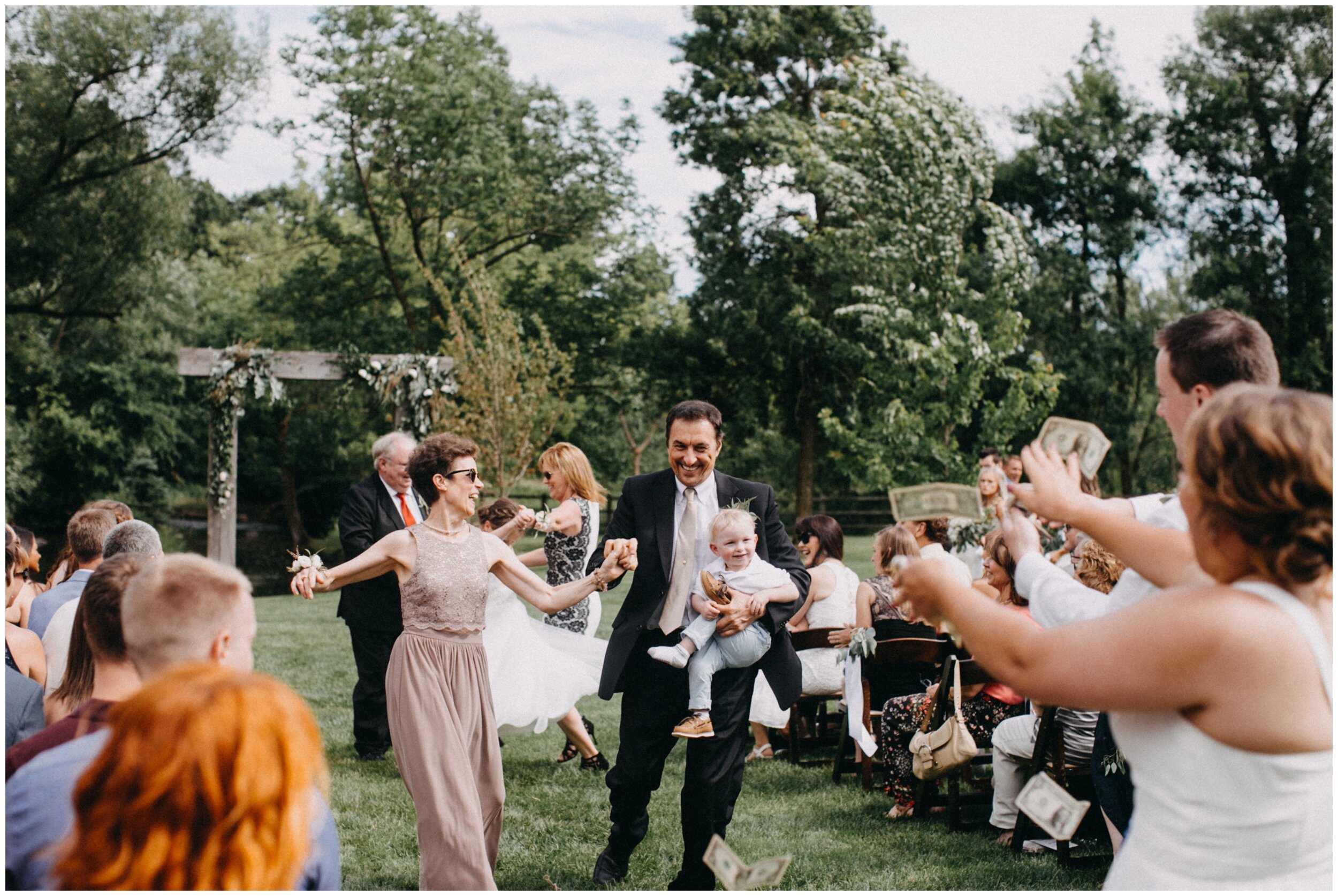 Groom's parents dancing down aisle and bridesmaid throwing money at them 