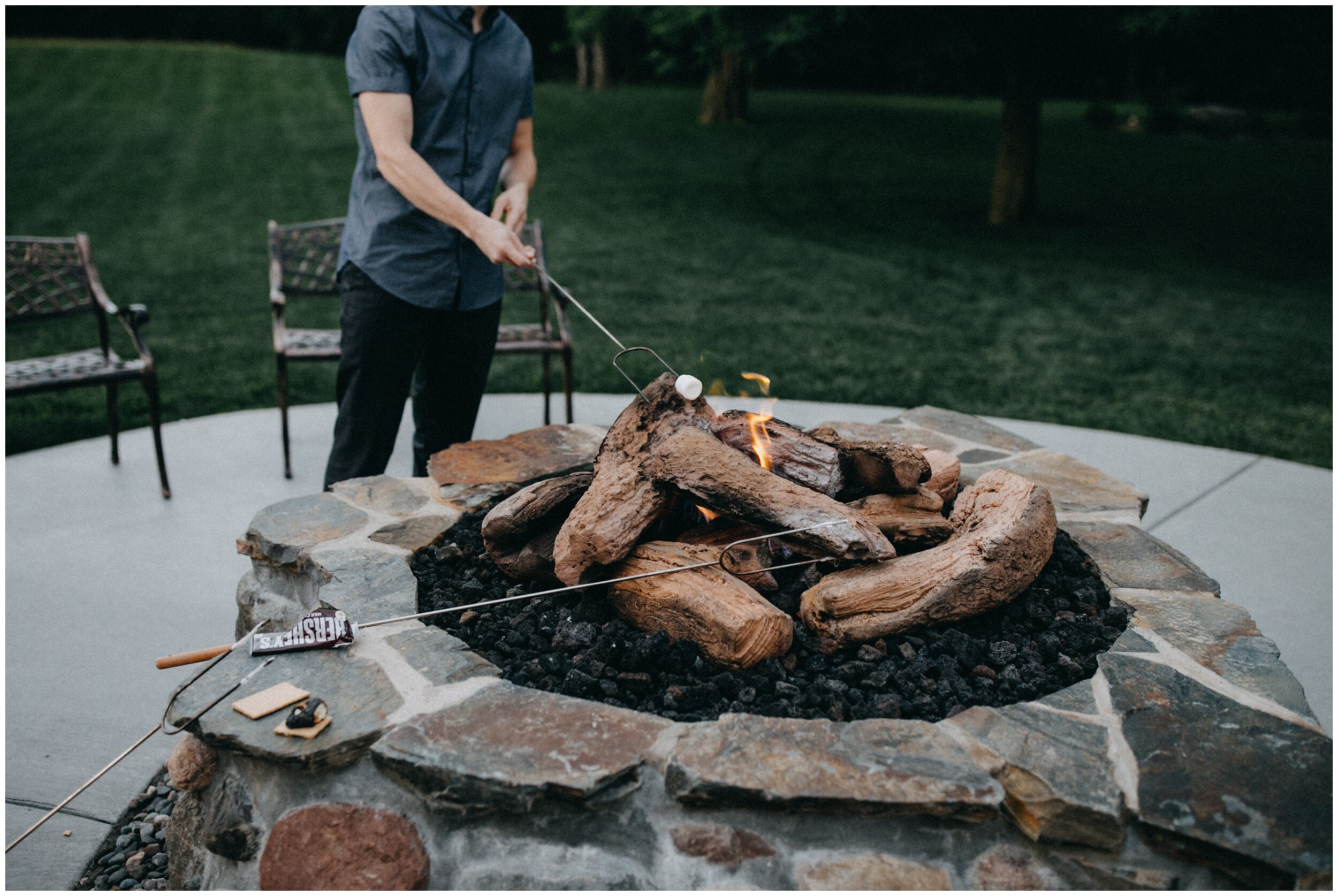 Guest roasting marshmallow over bonfire at outdoor barn wedding