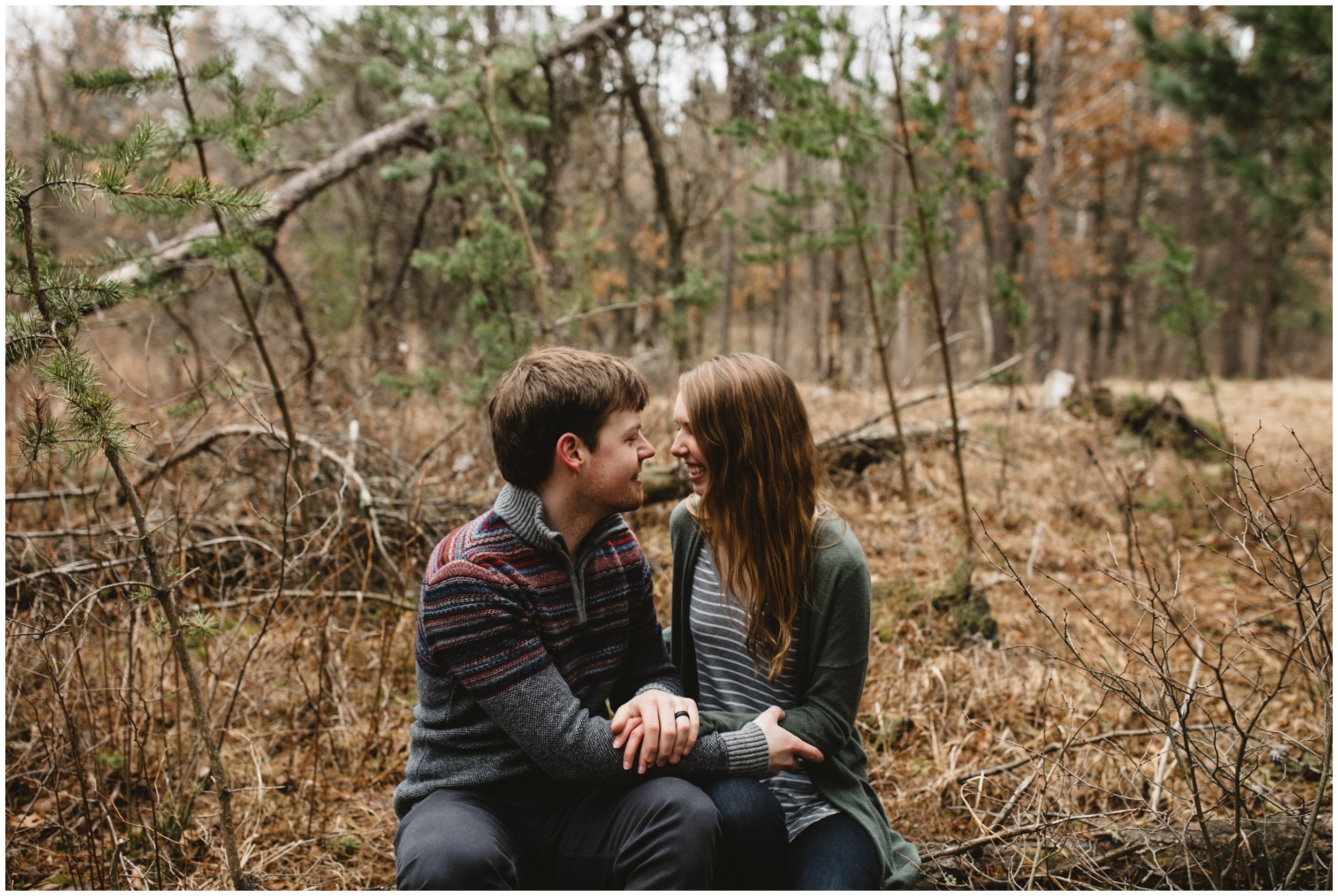 Couple sitting on log in the woods during Minnesota woodsy engagement session