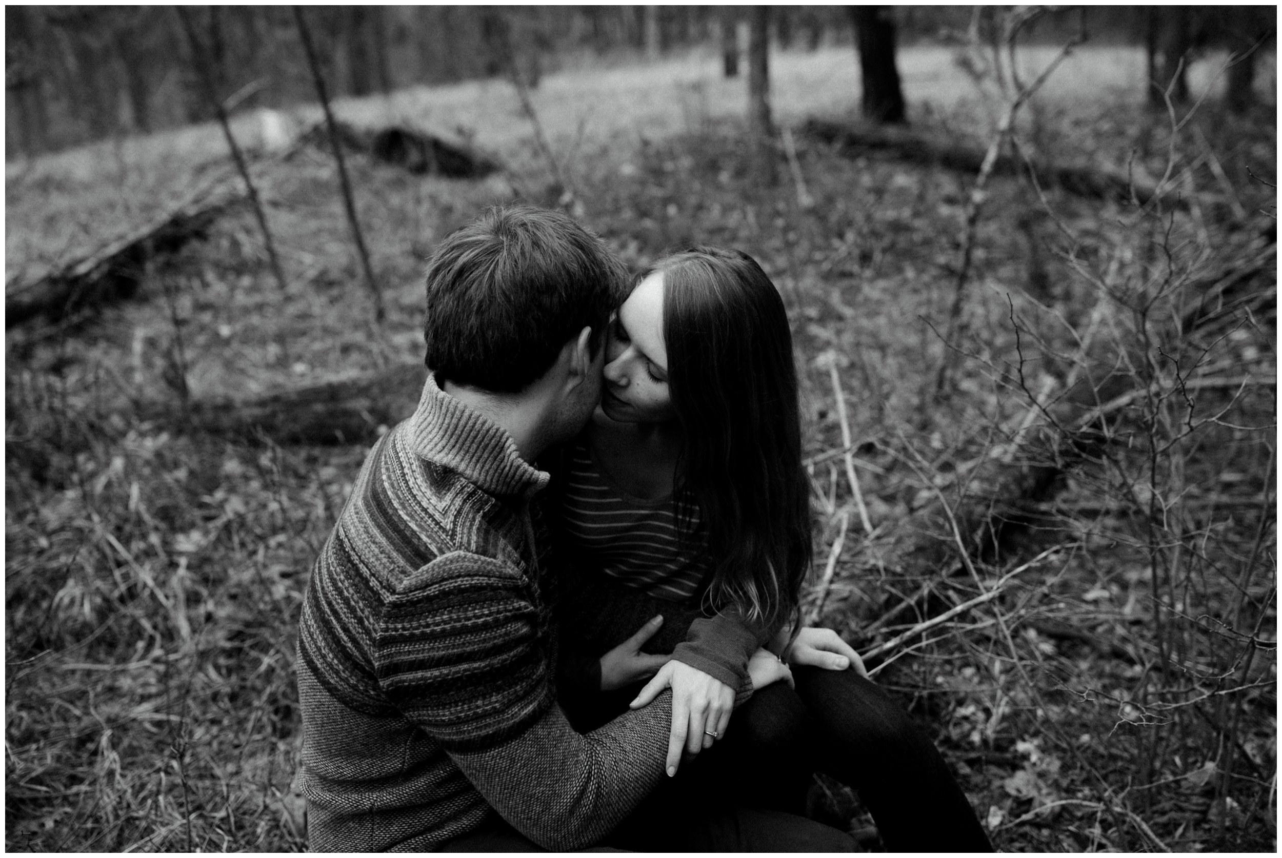 Couple hugging while sitting on log in the woods during Brainerd, Minnesota engagement session