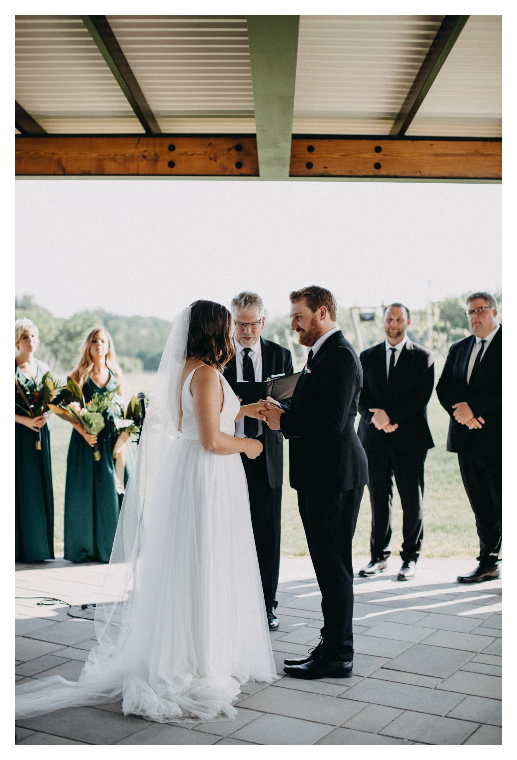 Bride and groom exchanging wedding bands during ceremony overlooking vineyard in Minnesota