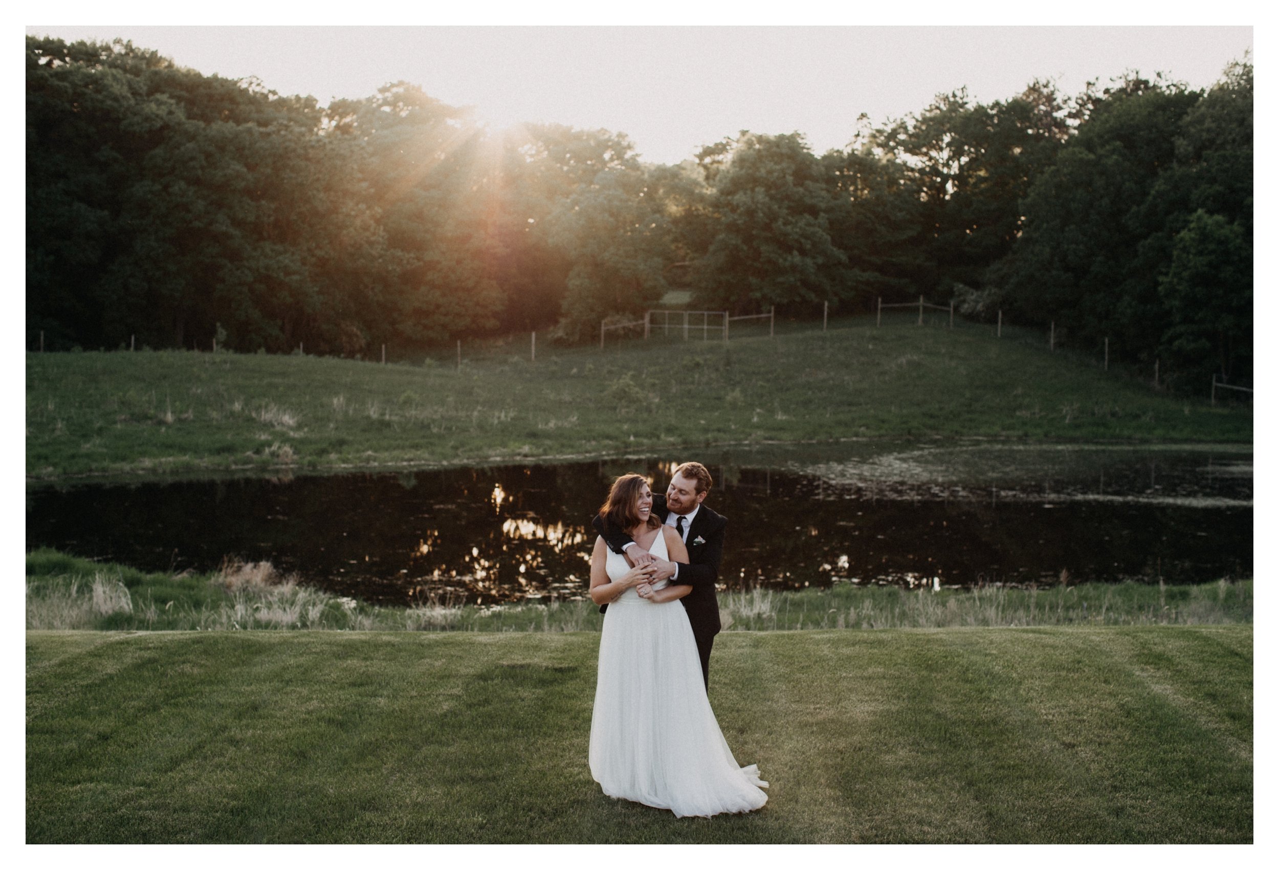 Bride and groom standing in front of pond overlooking Minnesota vineyard during sunset