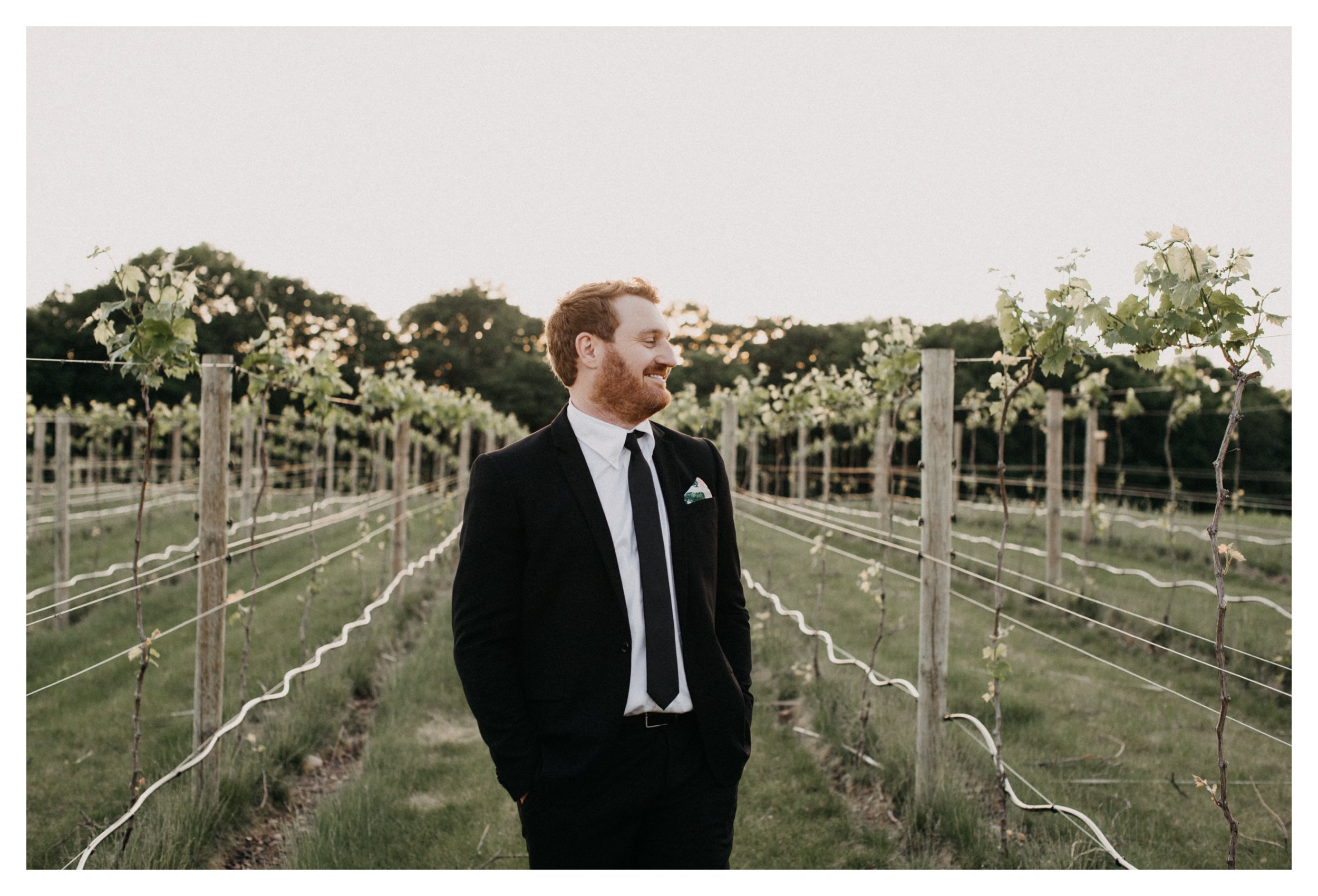 Groom standing in vineyard during sunset Minnesota winery wedding