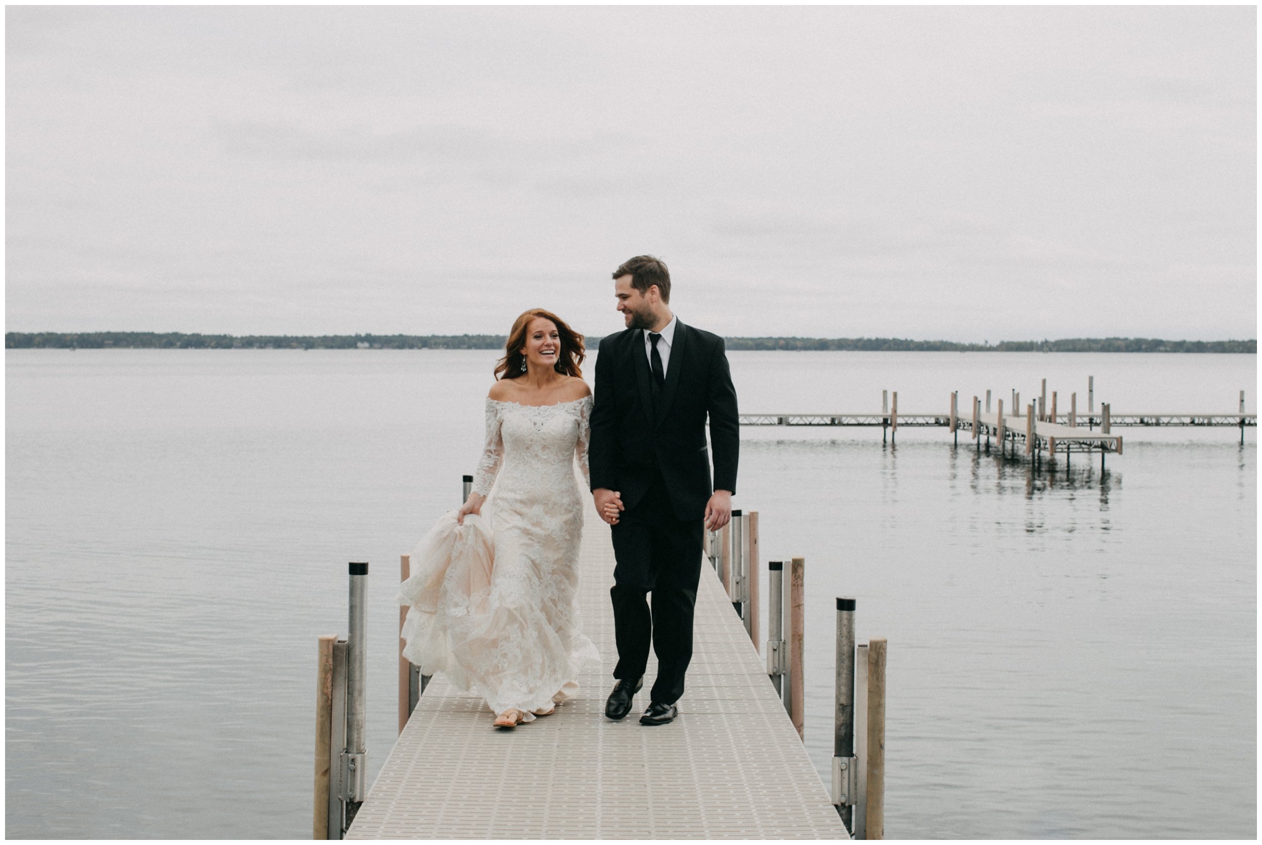Bride and groom holding hands and smiling, walking on dock on Gull Lake in Nisswa, Minnesota