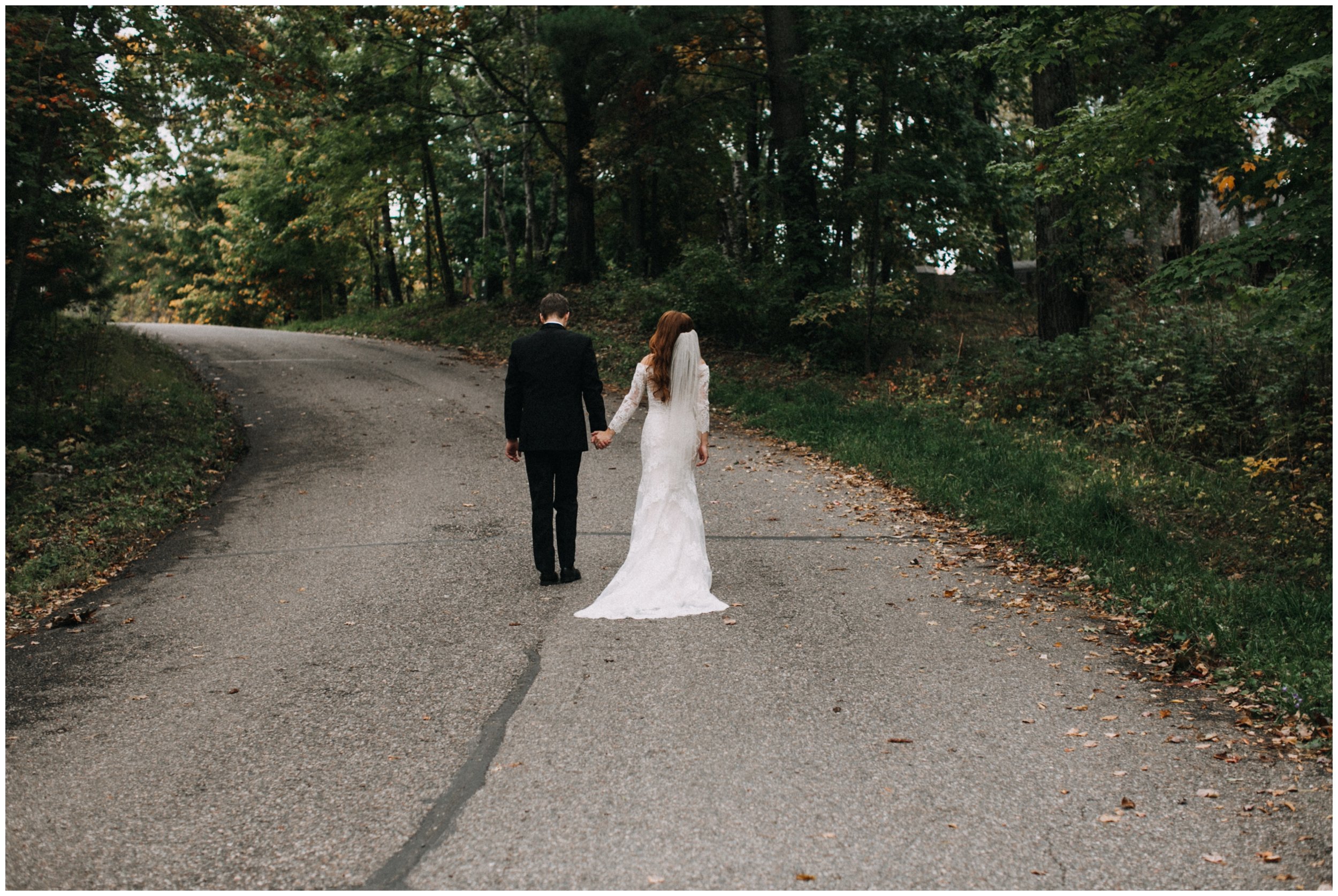 Bride and groom holding hands, walking on wooded road in Nisswa, Minnesota