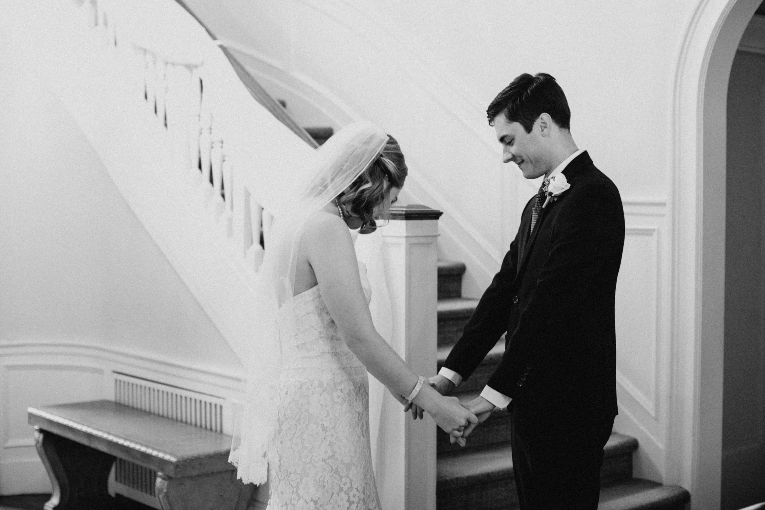 Bride wearing a timeless lace wedding dress and veil, holding hands with groom in front of staircase at the St Paul College Club