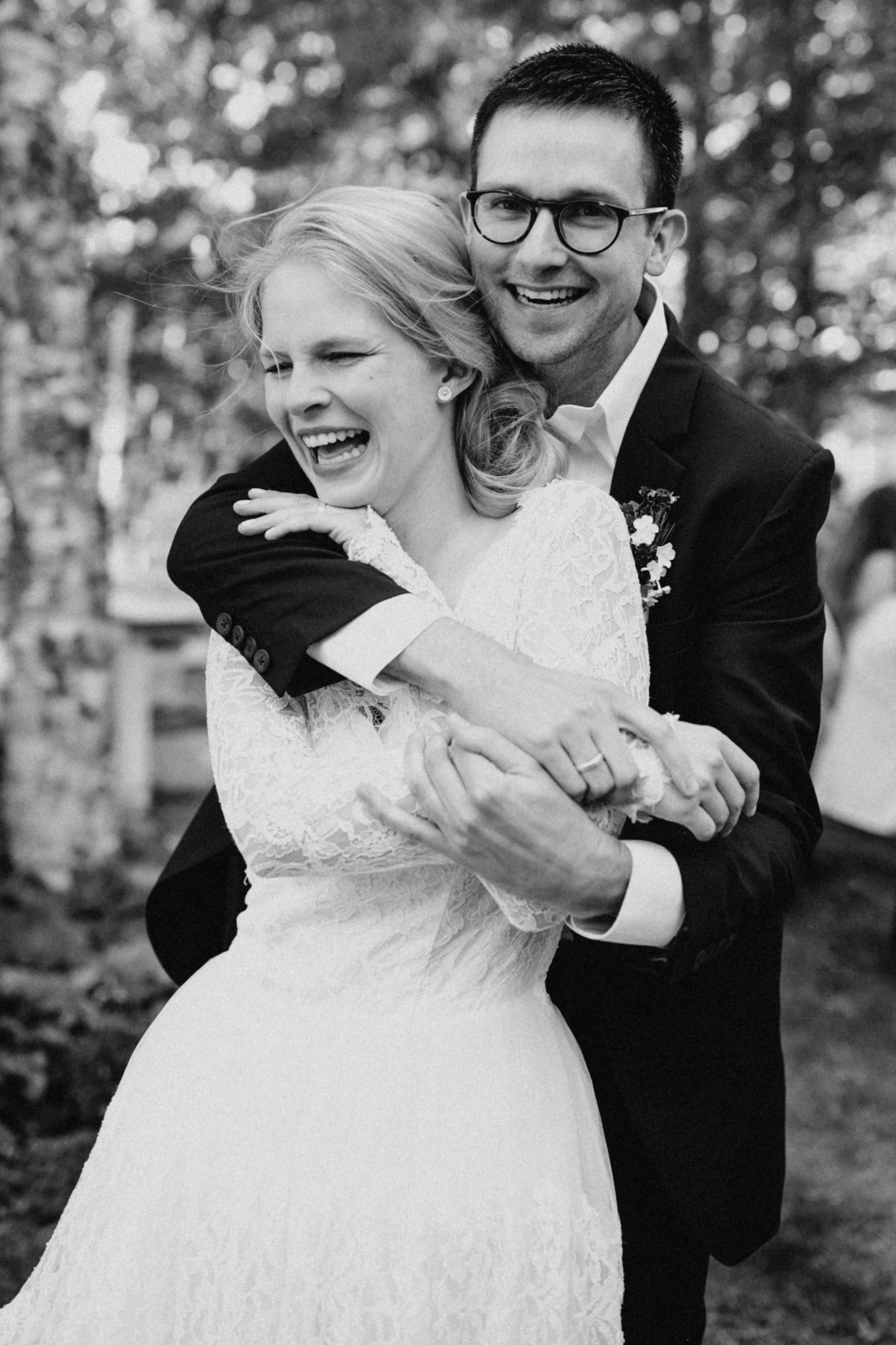 Groom wrapping his arms around the bride from behind as they both laugh during the cabin wedding in Minnesota