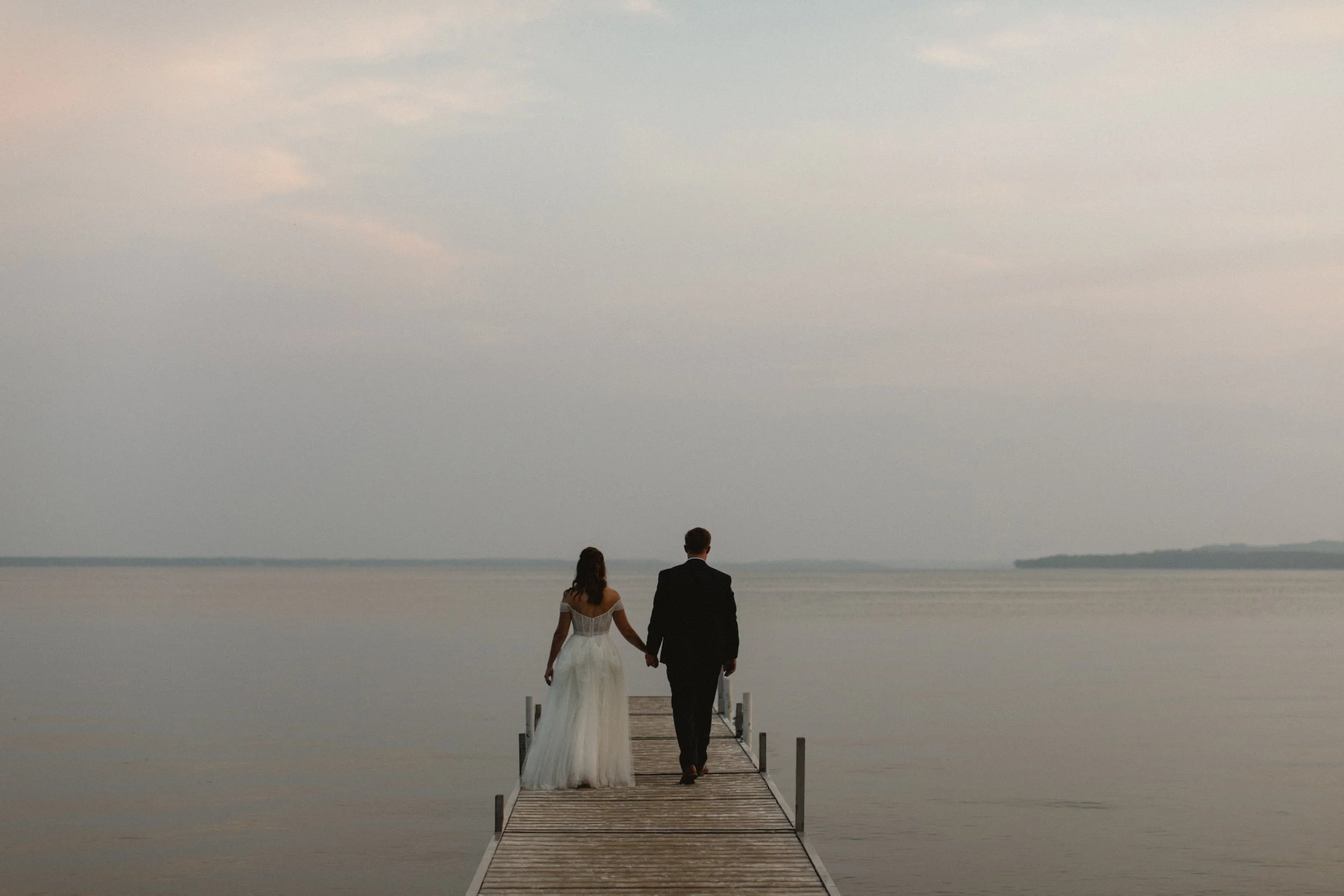 Bride and groom walking along dock during sunset on Gull Lake in Nisswa, Minnesota