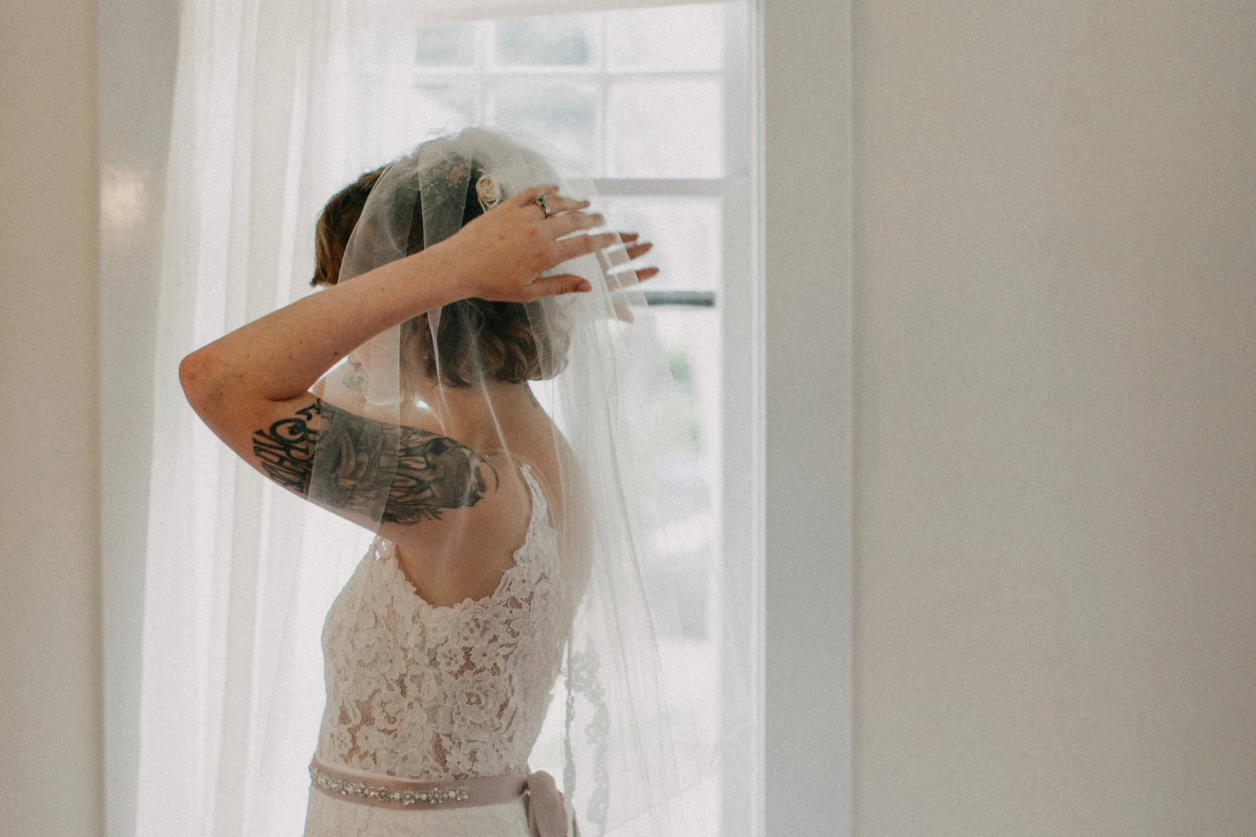 Bride with large arm tattoo putting on bridal veil before her wedding ceremony in Duluth, Minnesota