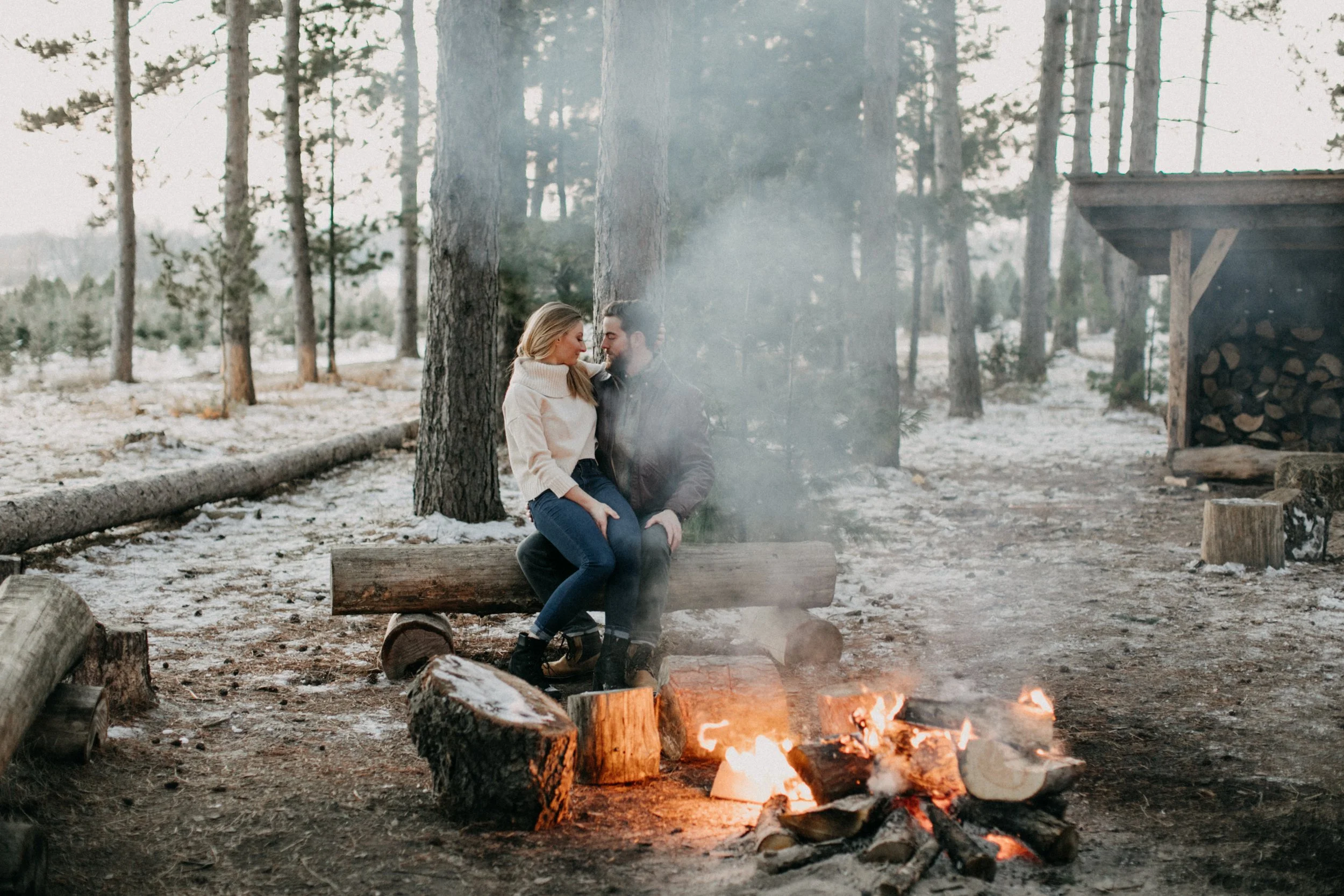 Couple cuddling in front of a bonfire surrounded by pine trees at Hanson Tree Farm in Minnesota