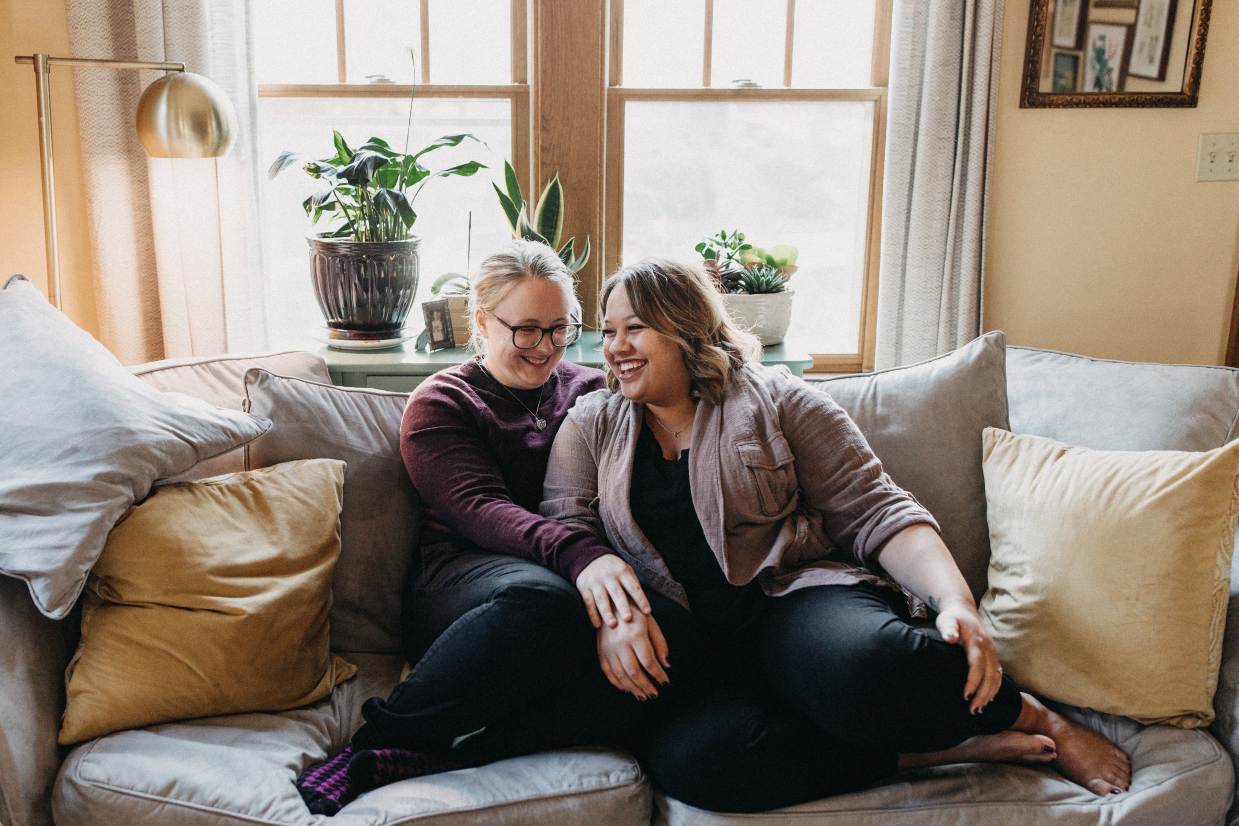 Engaged couple laughing, cuddled up on their couch at their home in Minneapolis.