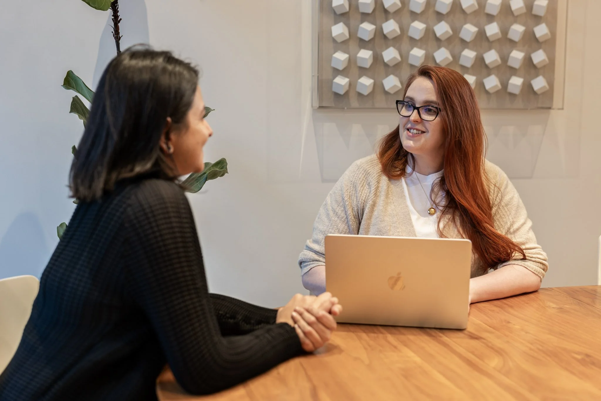 Two women are talking with a laptop between them.