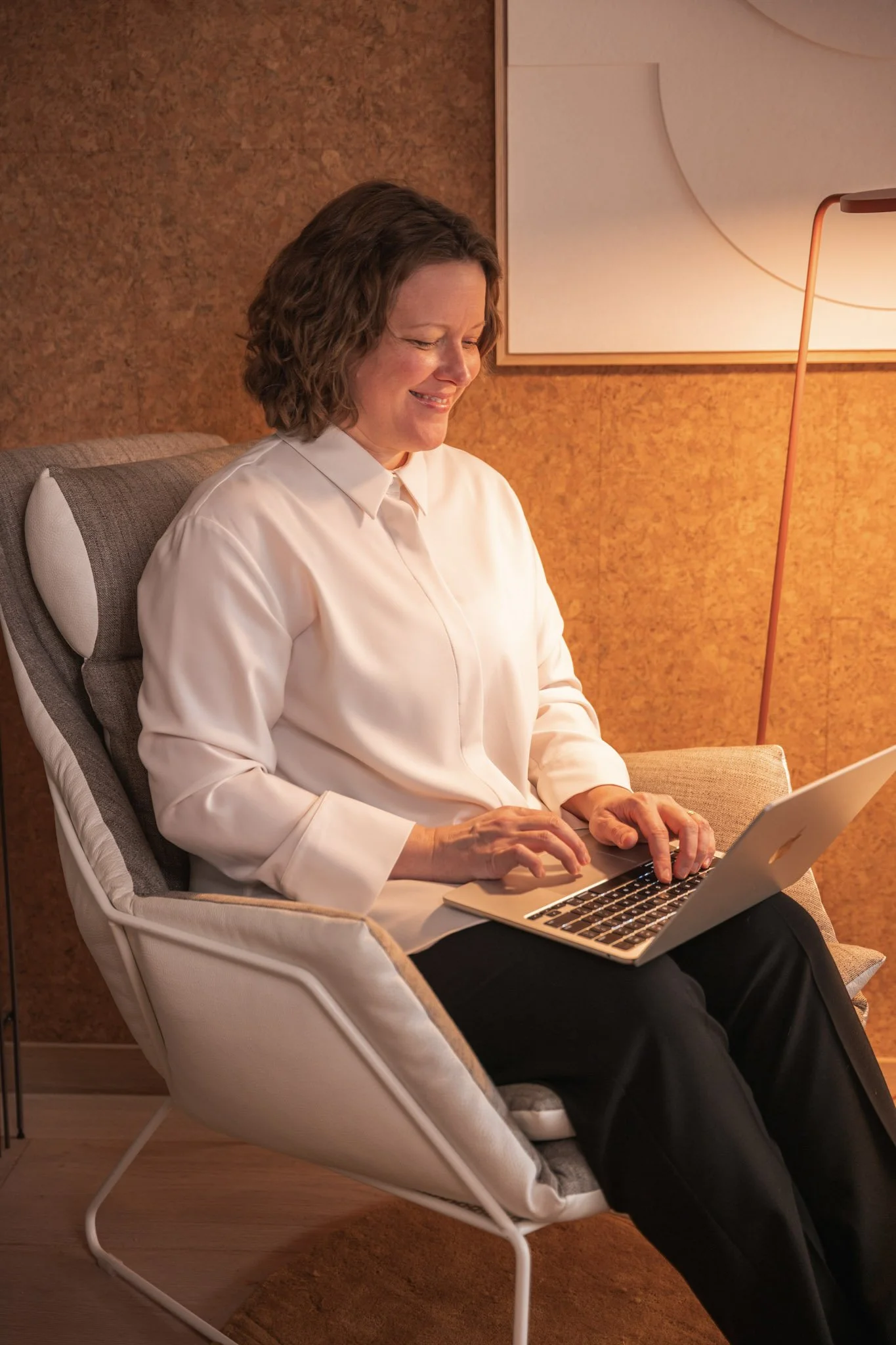 A woman works on a laptop beneath a lamp
