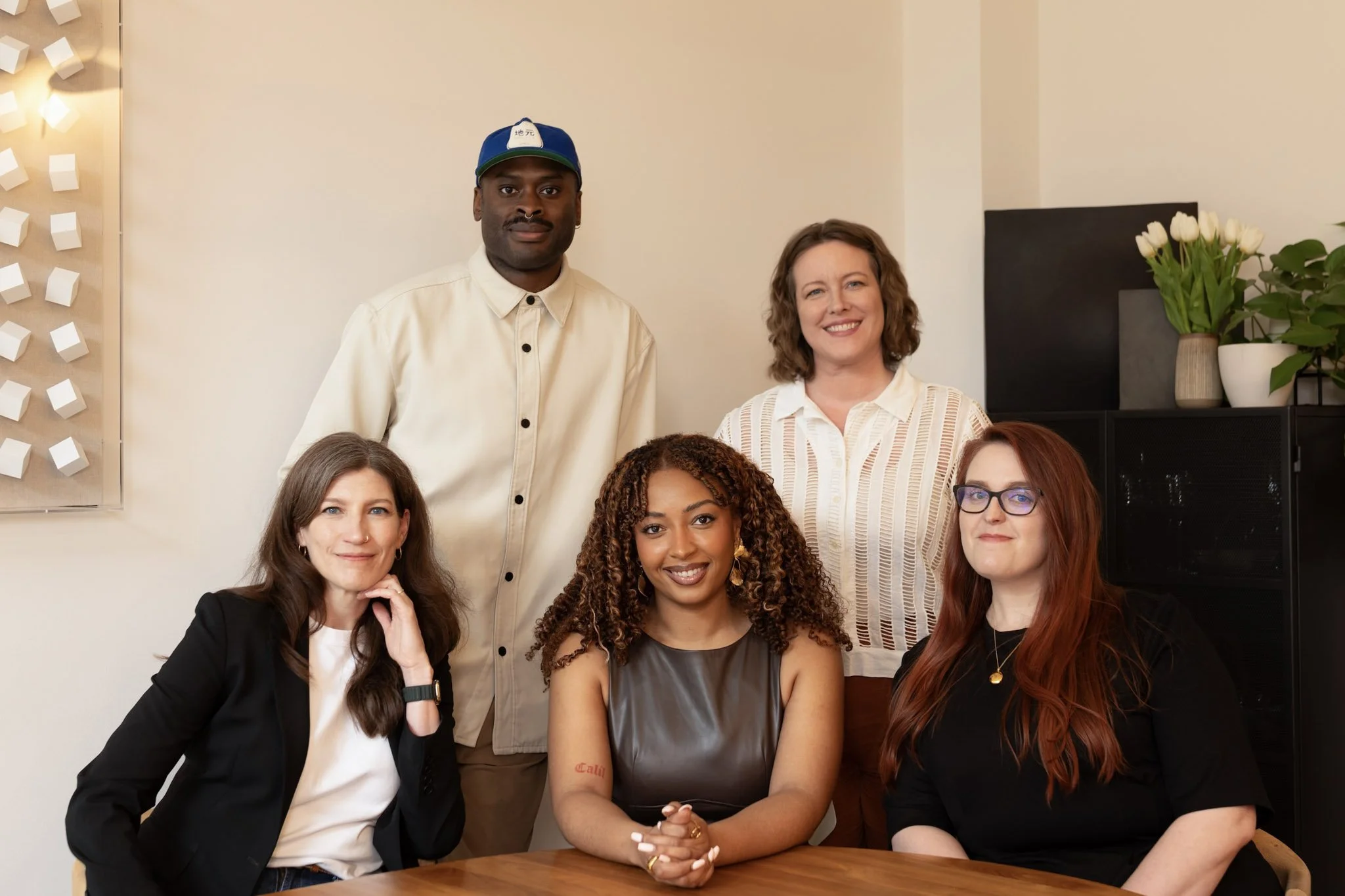 Five people stand and sit around a desk.