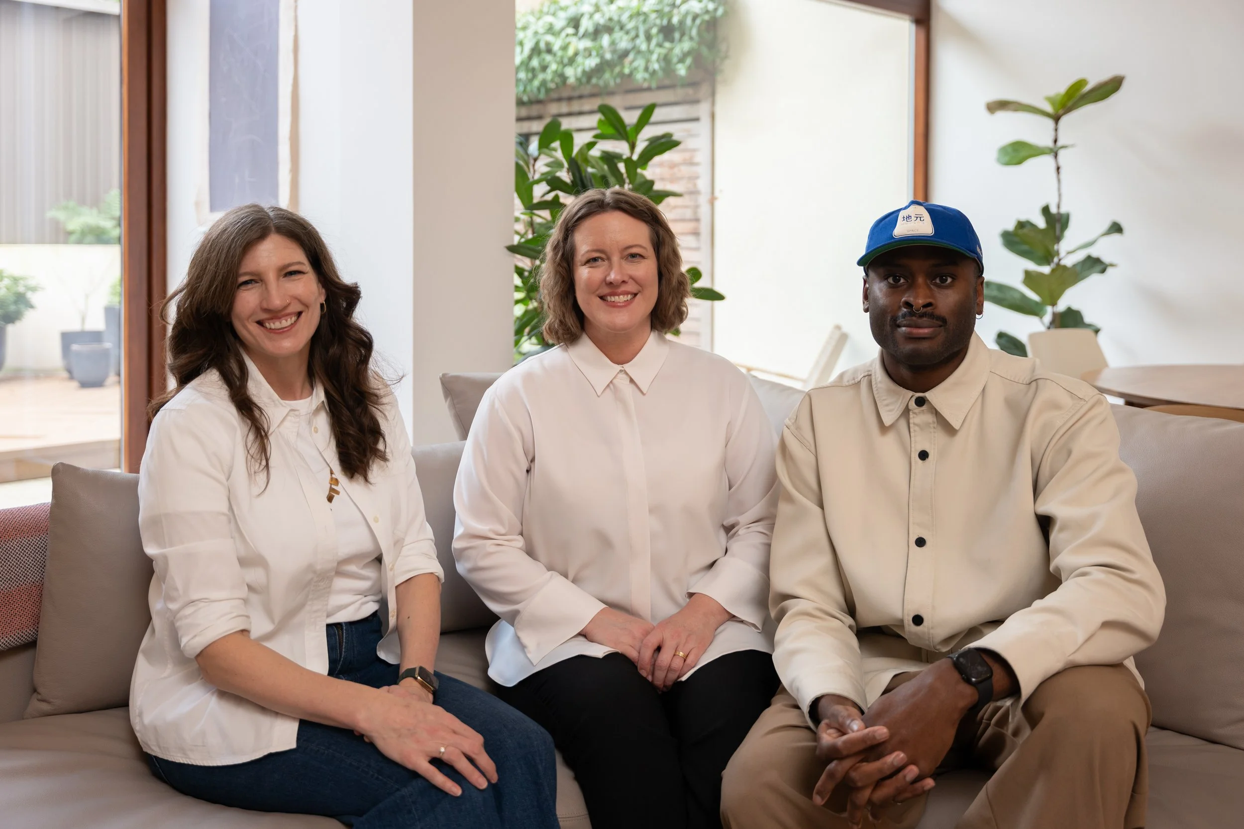 Three people wearing informal business attire  sit on a sofa.