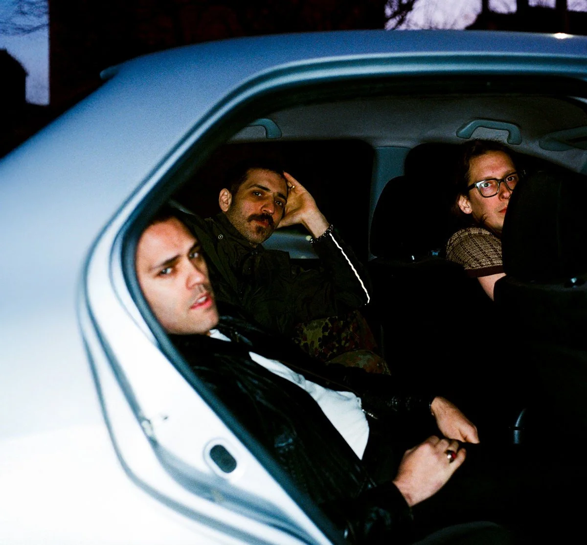 The members of Bambara sit in the back seat of a car; photo is taken from outside the open door.