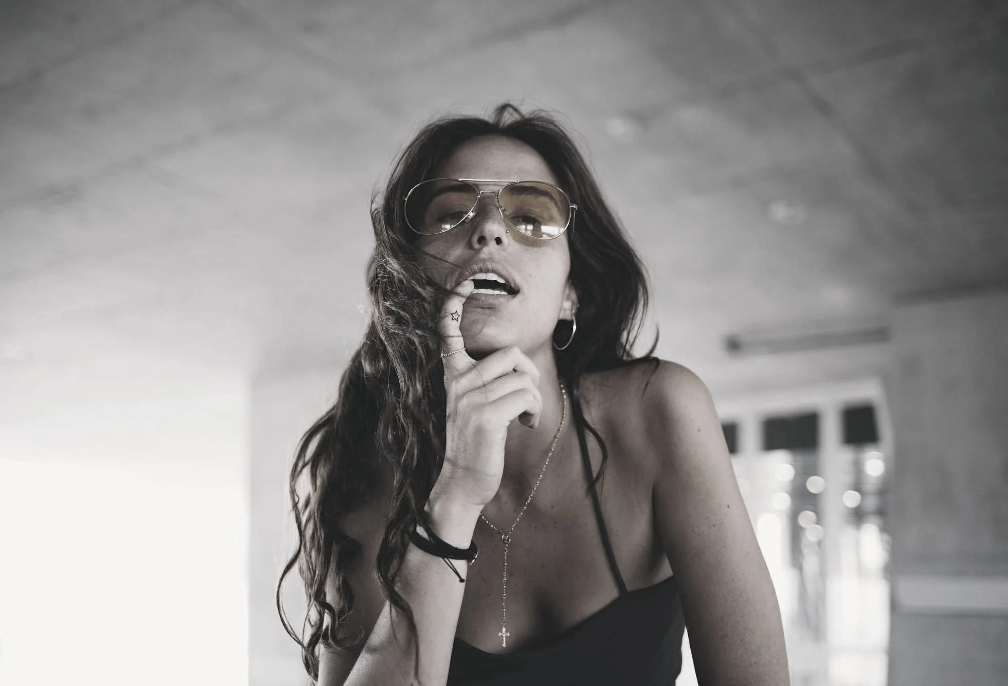 Woman with long hair and glasses looking directly at camera with fore finger at side of mouth