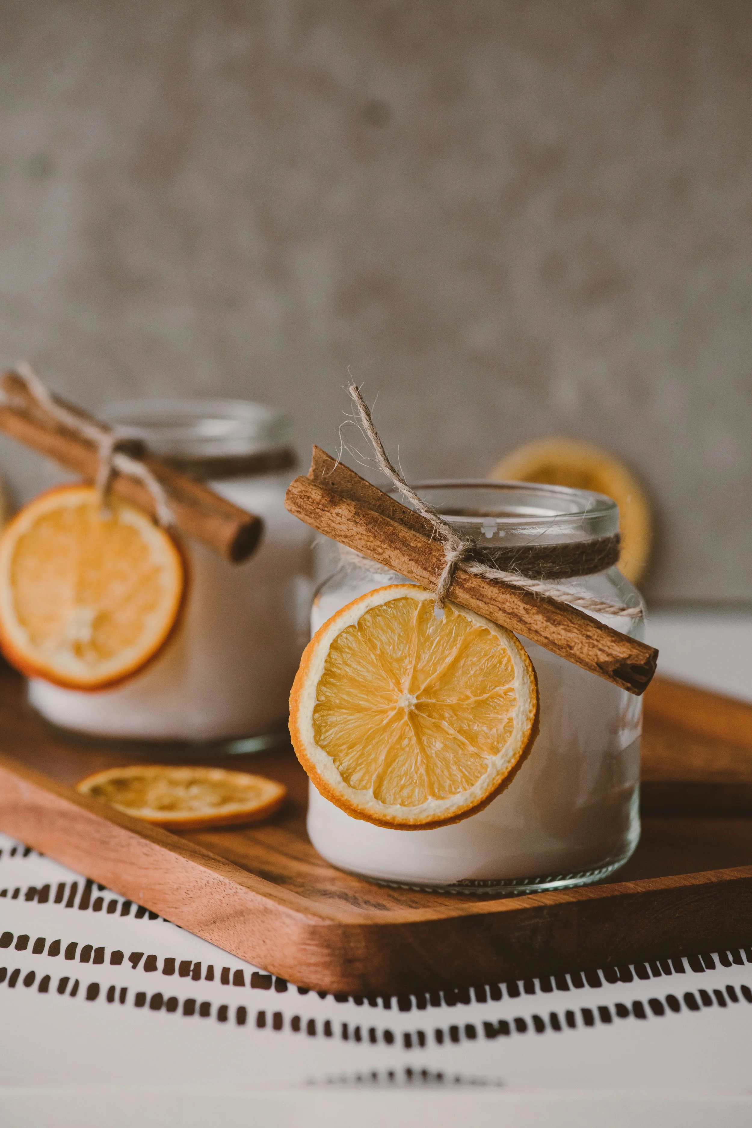 Glass jars of homemade candles decorated with dried orange slices and cinnamon sticks on a wooden tray — a warm, calming image for a blog on how to recover from autistic burnout.