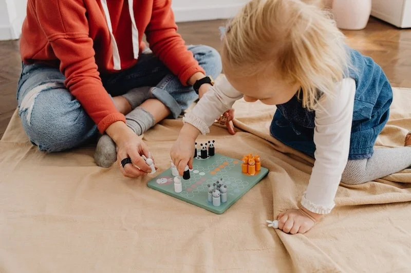 Comment aider son enfant à se faire des amis ? Un adulte et un enfant jouent à un jeu de société, une situation où l'on apprend à perdre, à attendre son tour, etc.