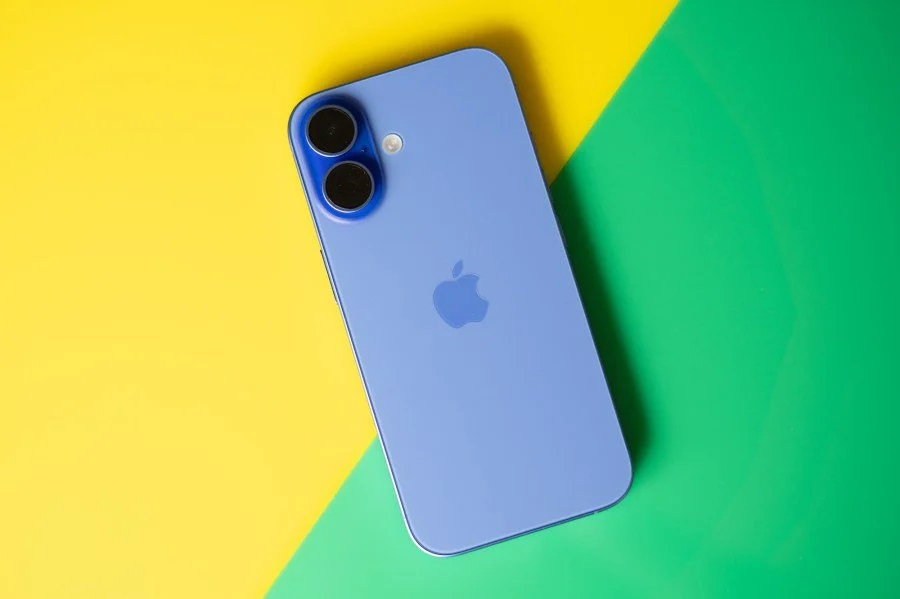 Blue iPhone 16 on yellow and green backgrounds, photographed by Allison Johnson / The Verge