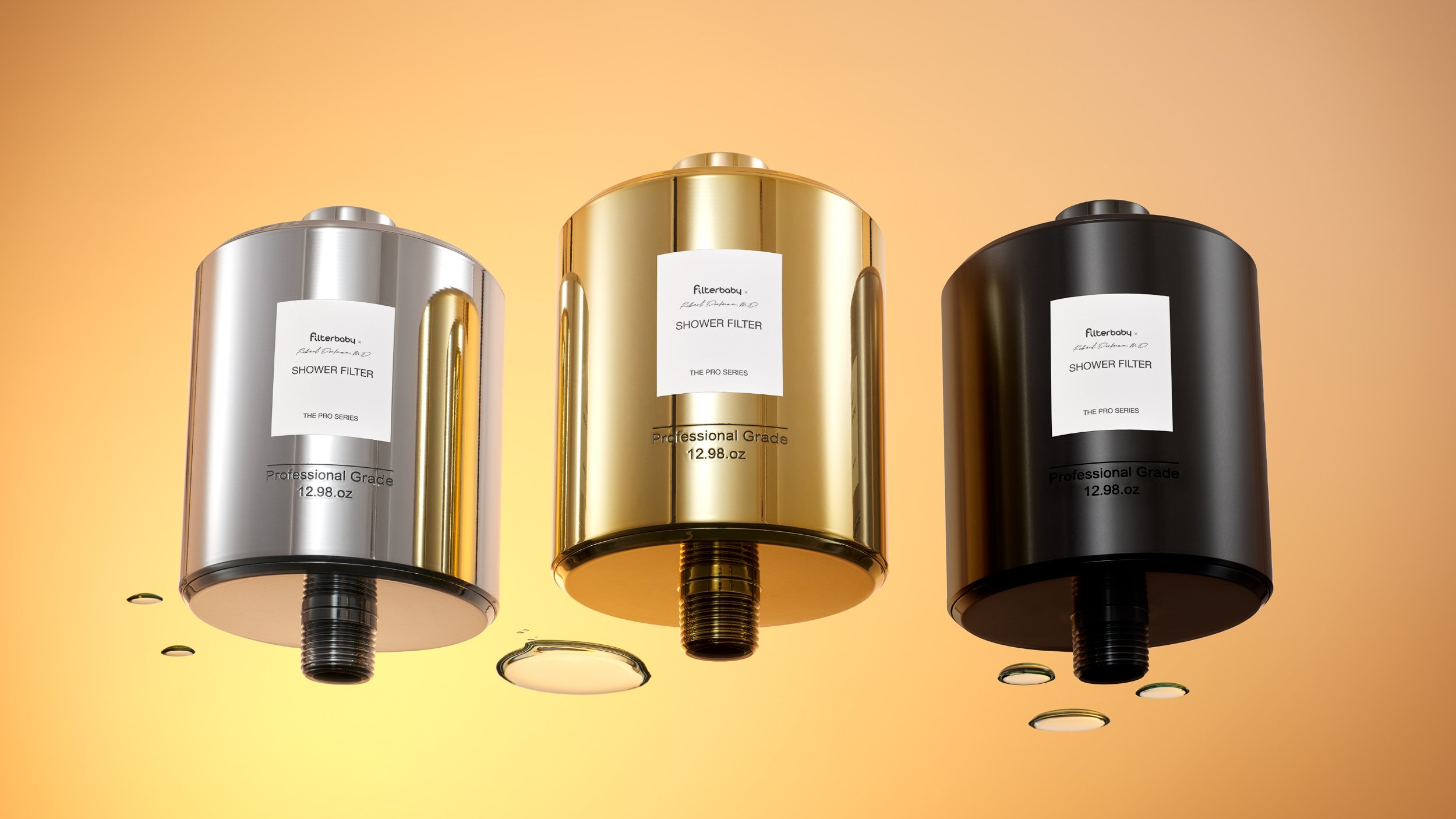 Filterbaby Pro shiny metal shower filter hero image with yellow and orange gradient background shot at a wide and low angle. The image shows all 3 colors, silver, gold, and black, and is styled with water drops on the surface.