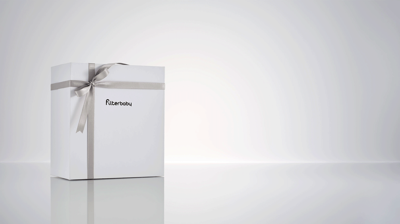 Stop motion animation GIF showing different bundle configurations for Filterbaby. A branded box with a gray satin bow sits on a light gray reflective surface with rotating bundles which include the Filterbaby Skincare Faucet Water Filters, Pro Series